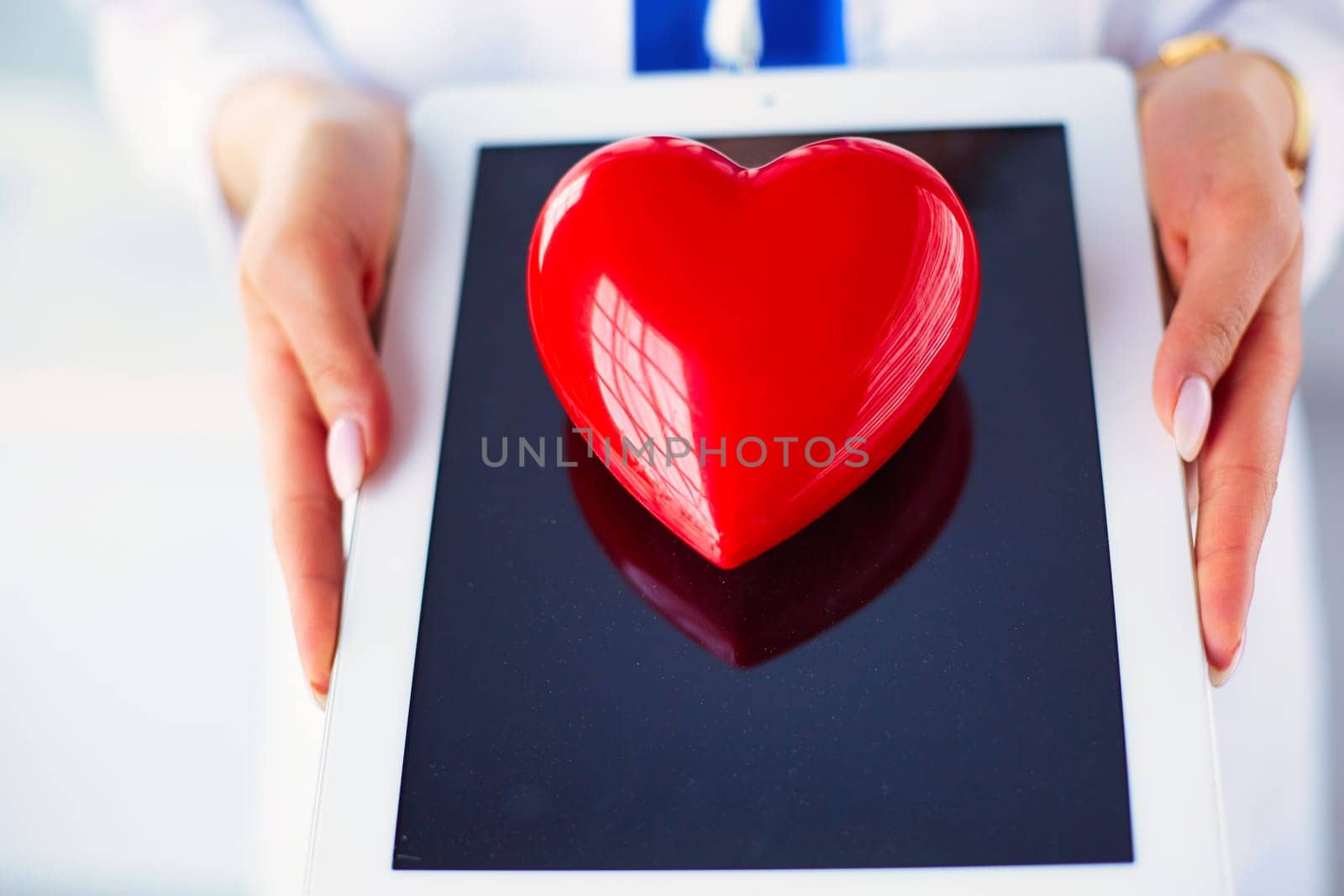 Female doctor with stethoscope holding heart, on light background.