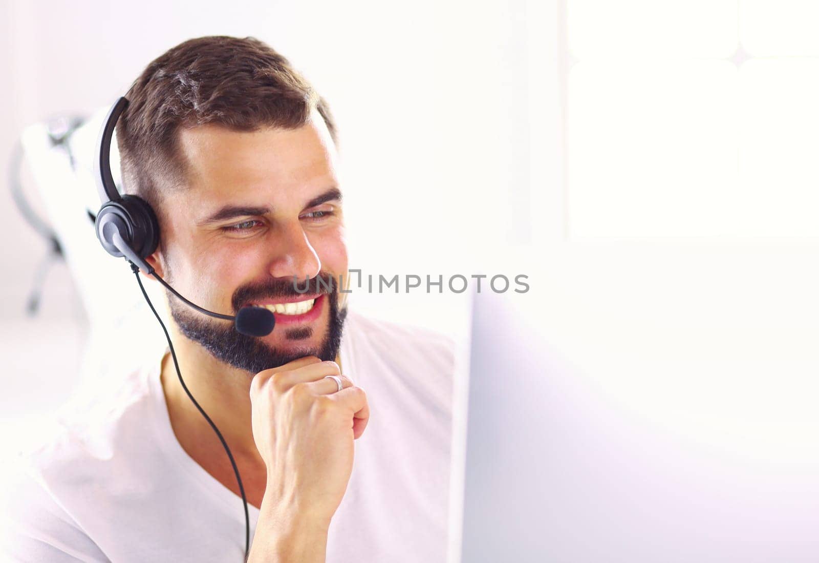 Portrait of a young man with a headset in front of a laptop computer.