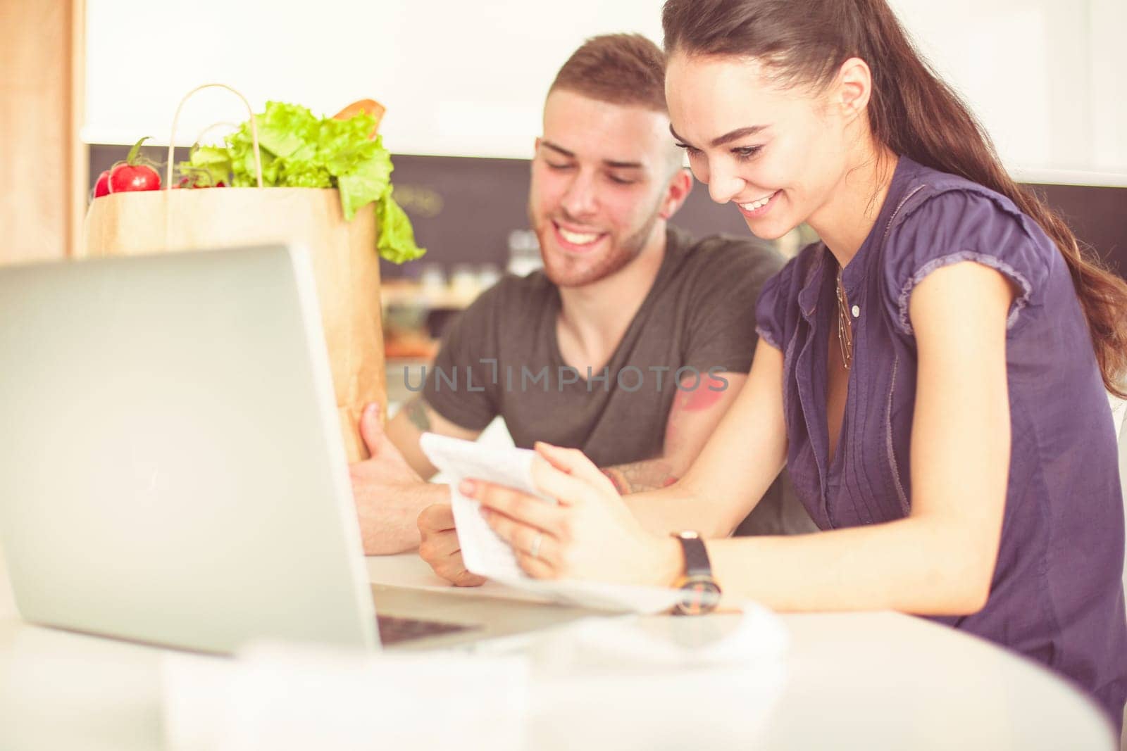 Couple paying their bills with laptop in kitchen at home.