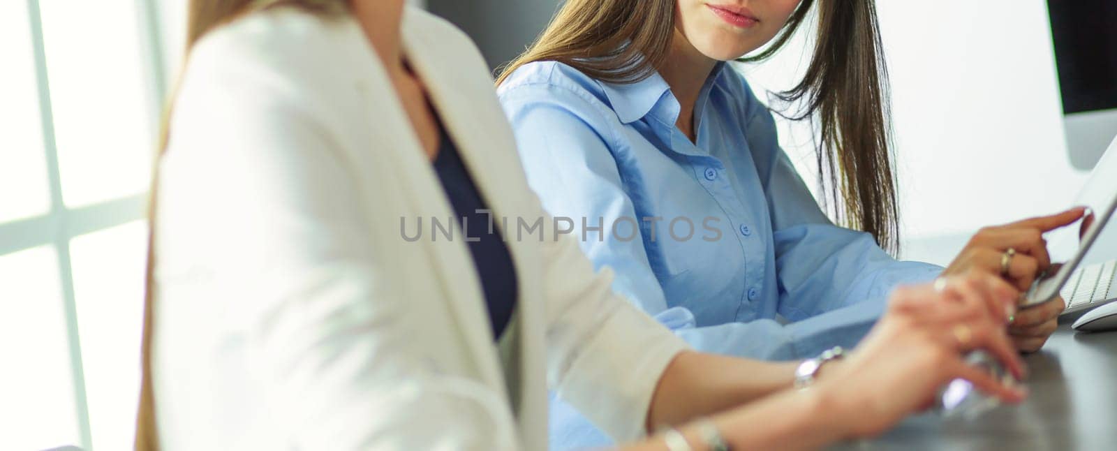 Two female colleagues in office sitting on the desk.