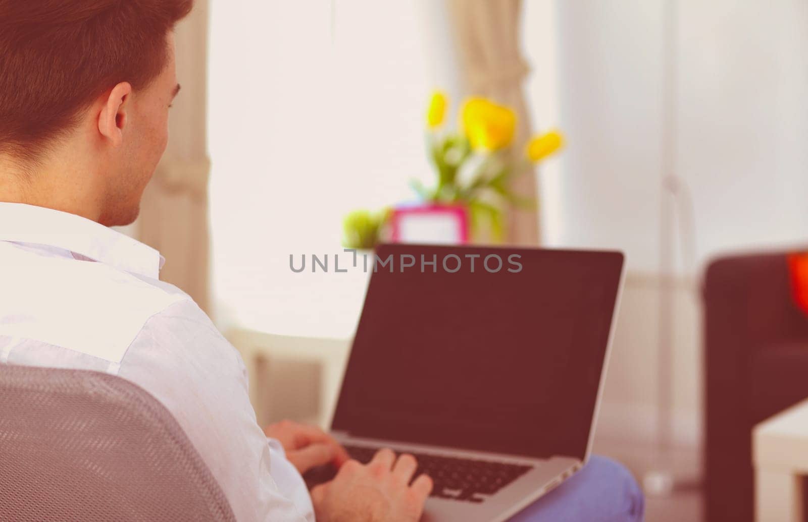 Happy man sitting on table and using laptop at home by lenets