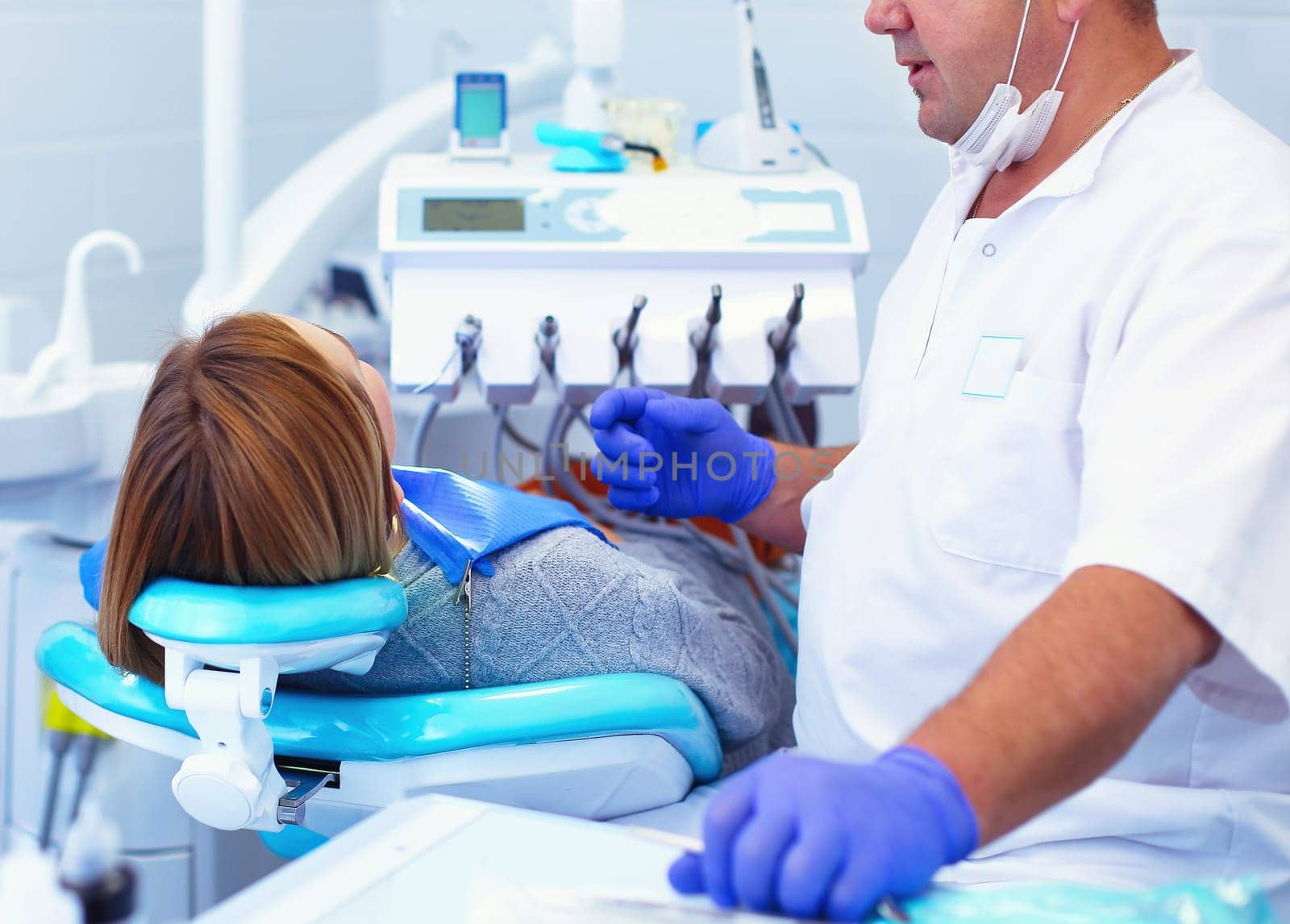 Senior male dentist in dental office talking with female patient and preparing for treatment.