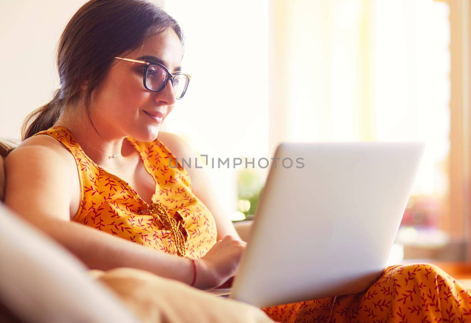 Young woman sitting on couch working on laptop computer at home.