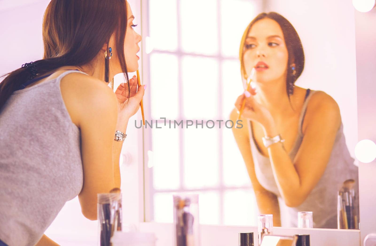 Young woman applying lipstick in front of a mirror.