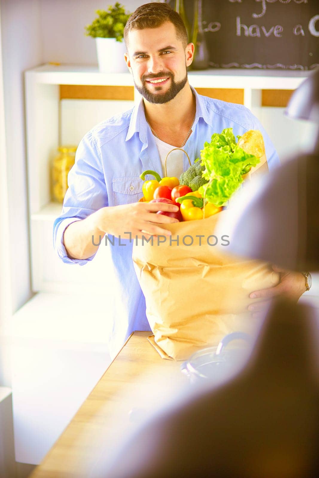 Man holding paper bag full of groceries on the kitchen background. Shopping and healthy food concept.