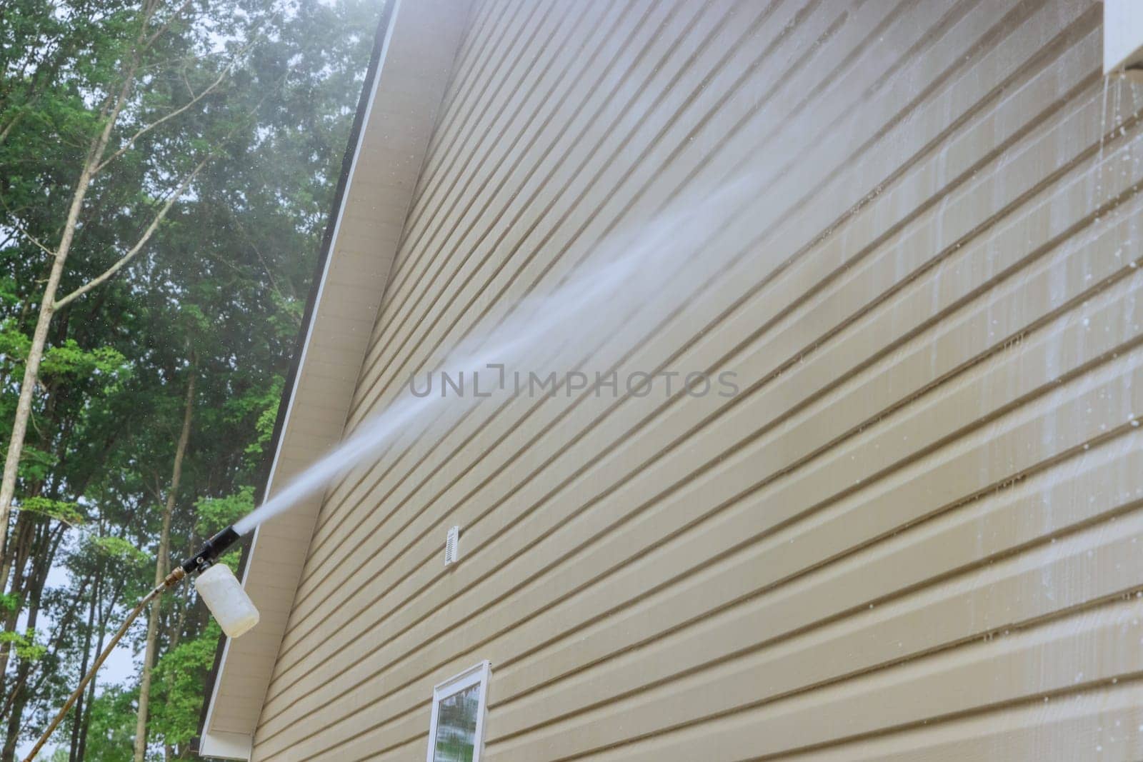 Service man in washing siding houses by using a high pressure nozzles spray water soap cleaner by ungvar