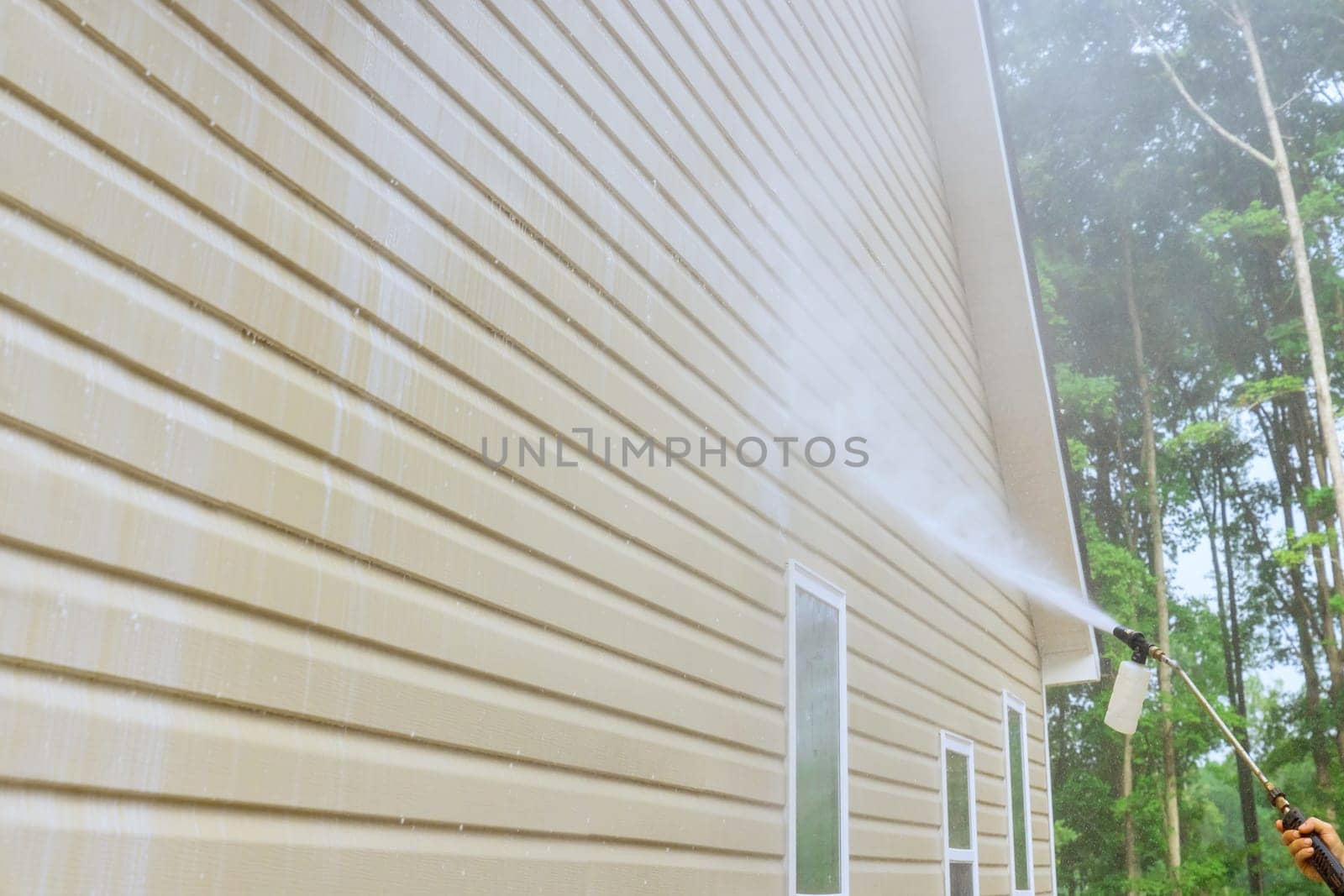 Service worker utilizes high pressure nozzles to efficiently clean siding houses with water soap cleaner.