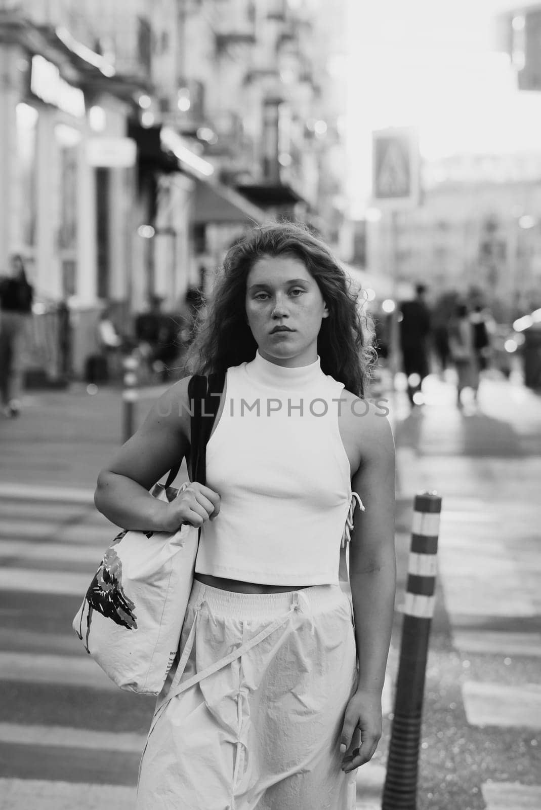 A stylish girl in white clothing with curly hair on the city streets. High quality photo