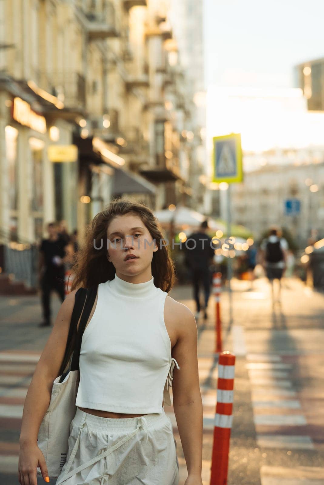 A stylish girl in white clothing with curly hair on the morning city streets. High quality photo