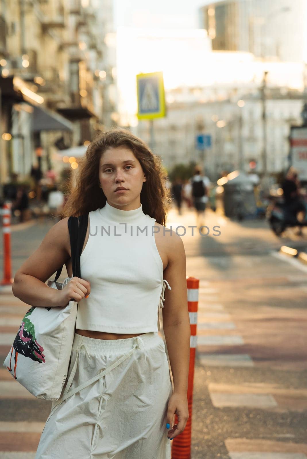 A chic girl wearing white clothes and sporting curly hair on the city streets. High quality photo