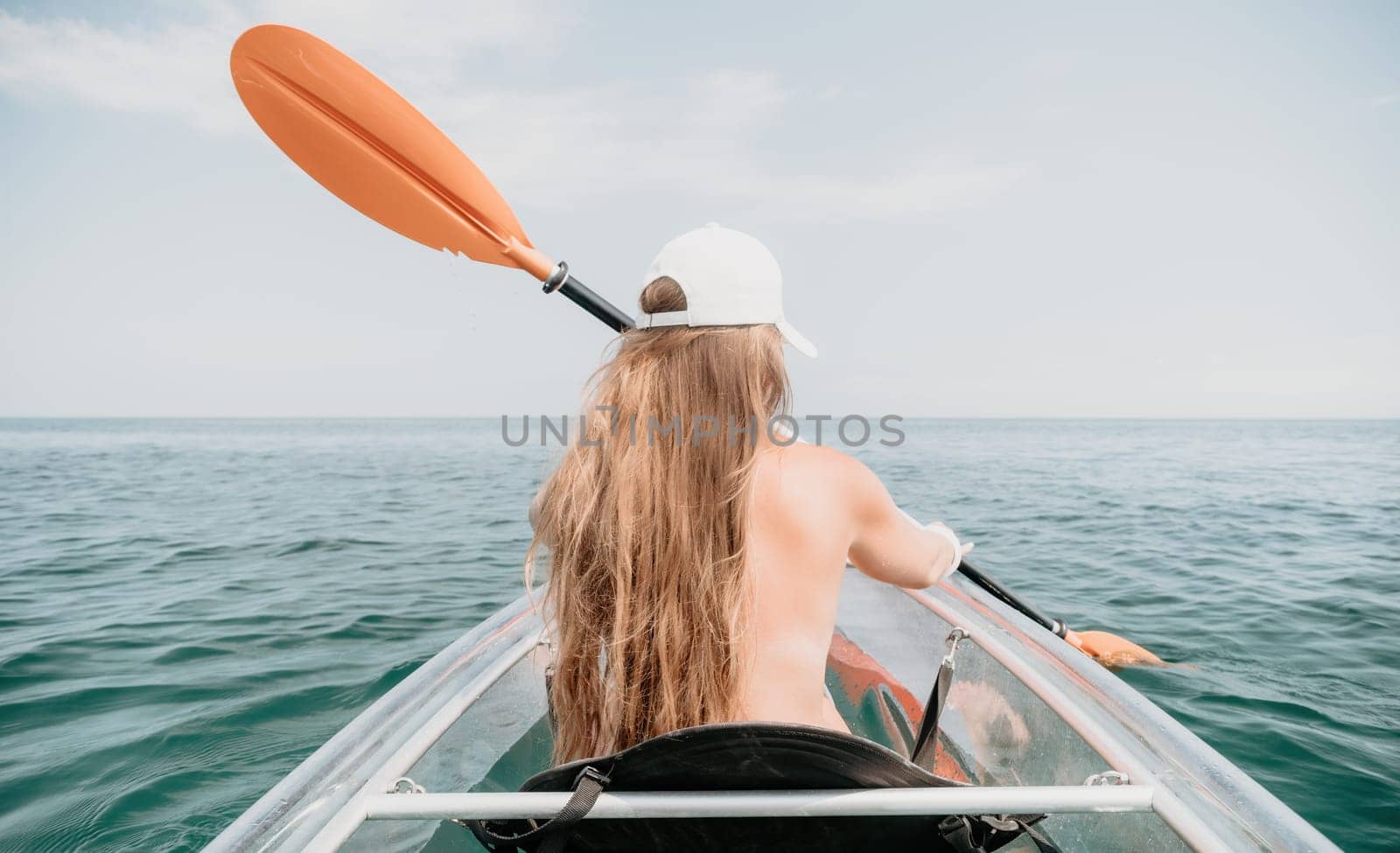 Woman in kayak back view. Happy young woman with long hair floating in transparent kayak on the crystal clear sea. Summer holiday vacation and cheerful female people having fun on the boat.