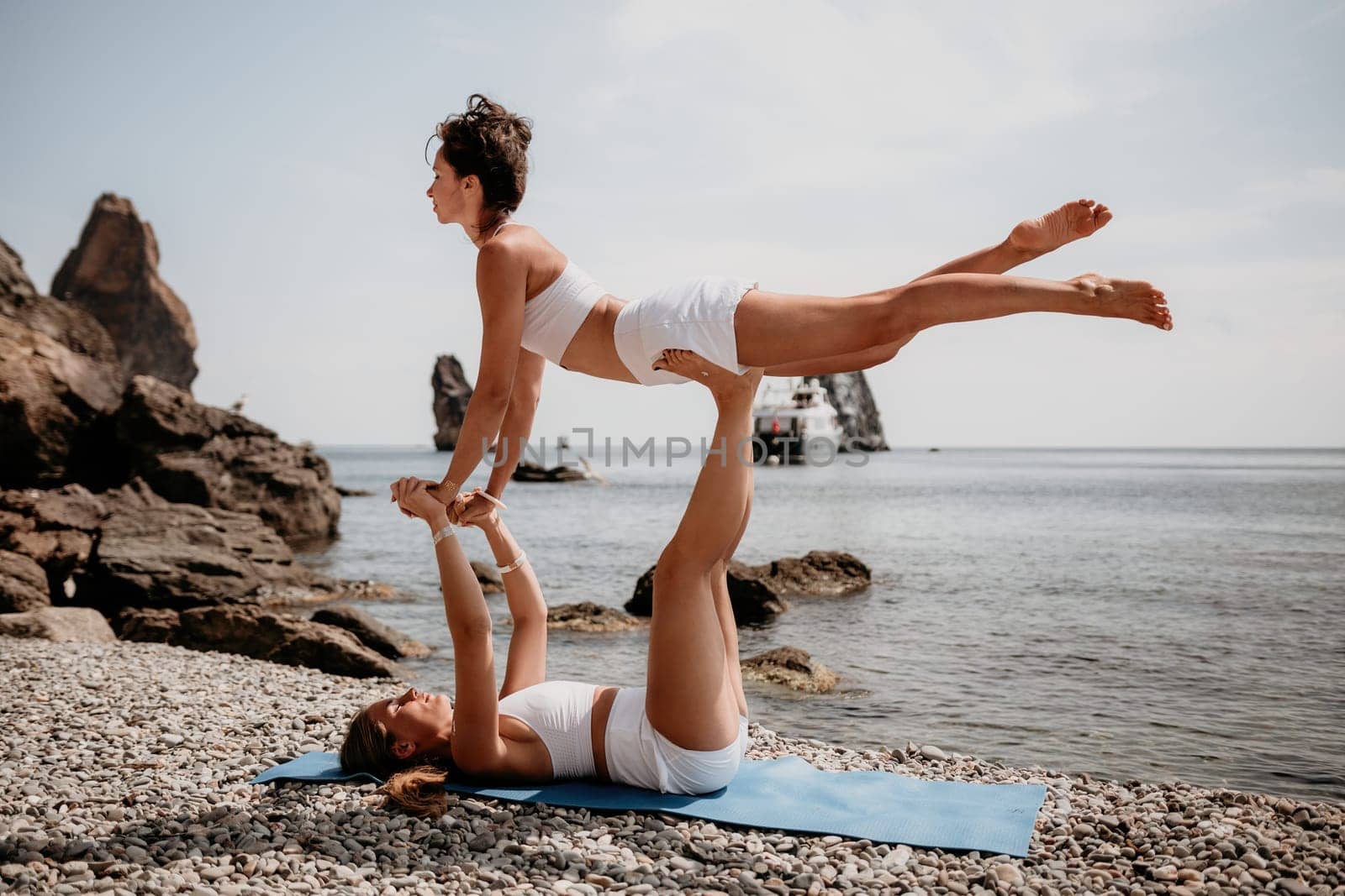 Woman sea yoga. Two Happy women meditating in yoga pose on the beach, ocean and rock mountains. Motivation and inspirational fit and exercising. Healthy lifestyle outdoors in nature, fitness concept. by panophotograph