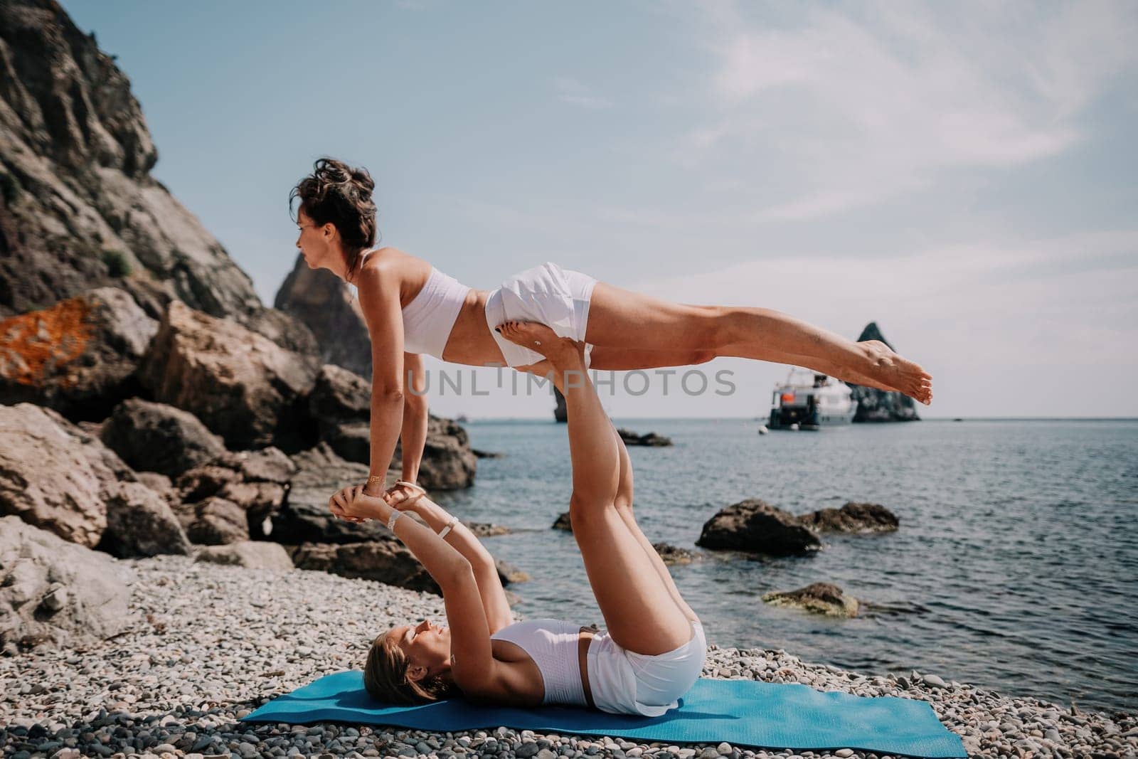 Woman sea yoga. Two Happy women meditating in yoga pose on the beach, ocean and rock mountains. Motivation and inspirational fit and exercising. Healthy lifestyle outdoors in nature, fitness concept. by panophotograph