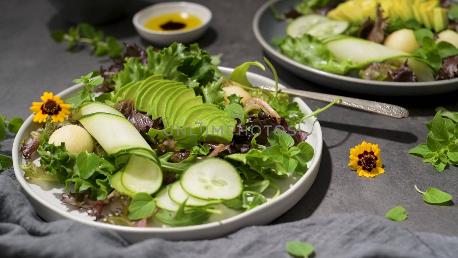 Fresh summer salad with cucumber, melon, avocado and fresh oregano served on ceramic plates.