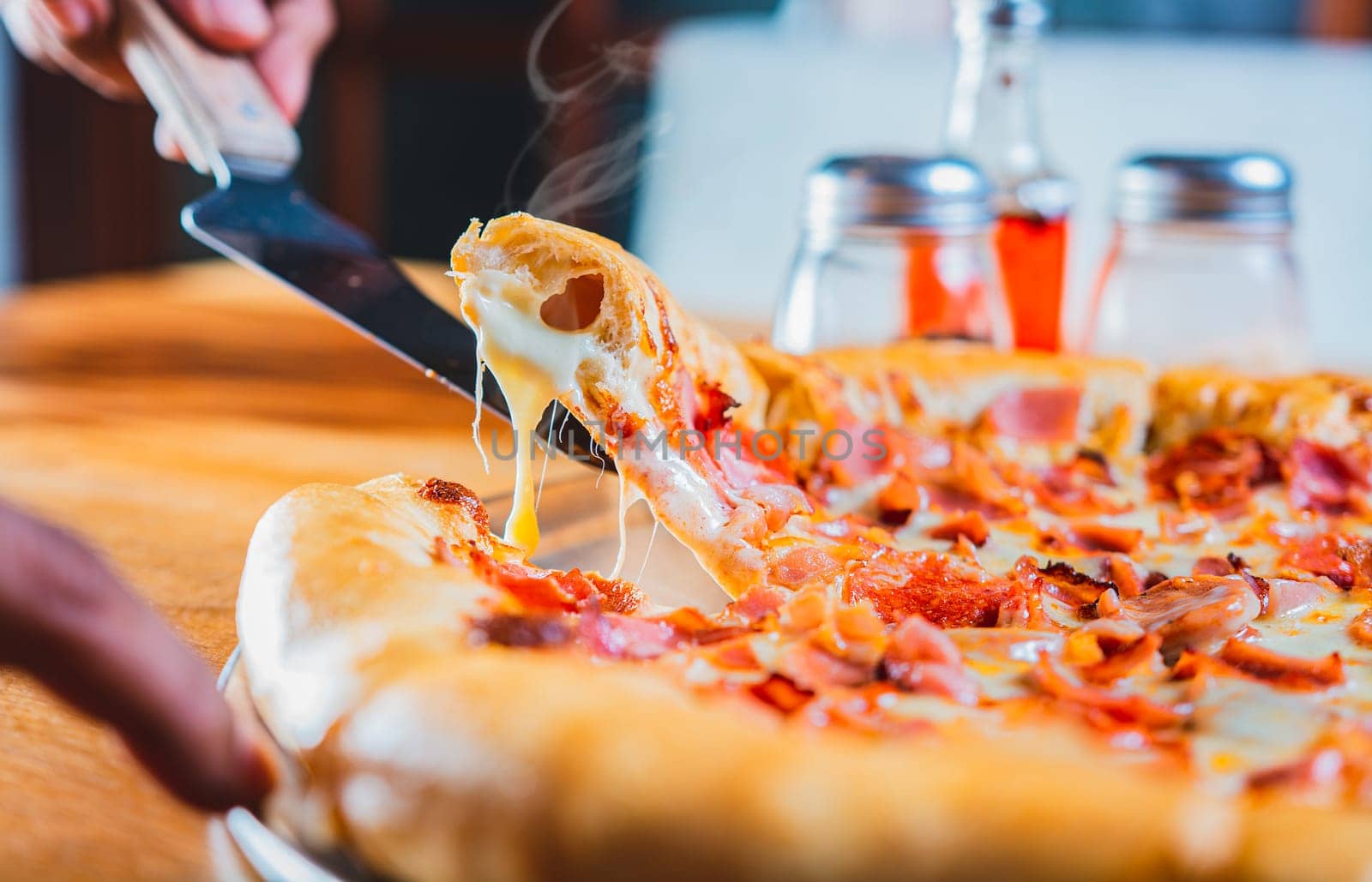 Hand taking a slice of ham pizza with the spatula. Person hand taking a slice of ham and cheese pizza with spatula