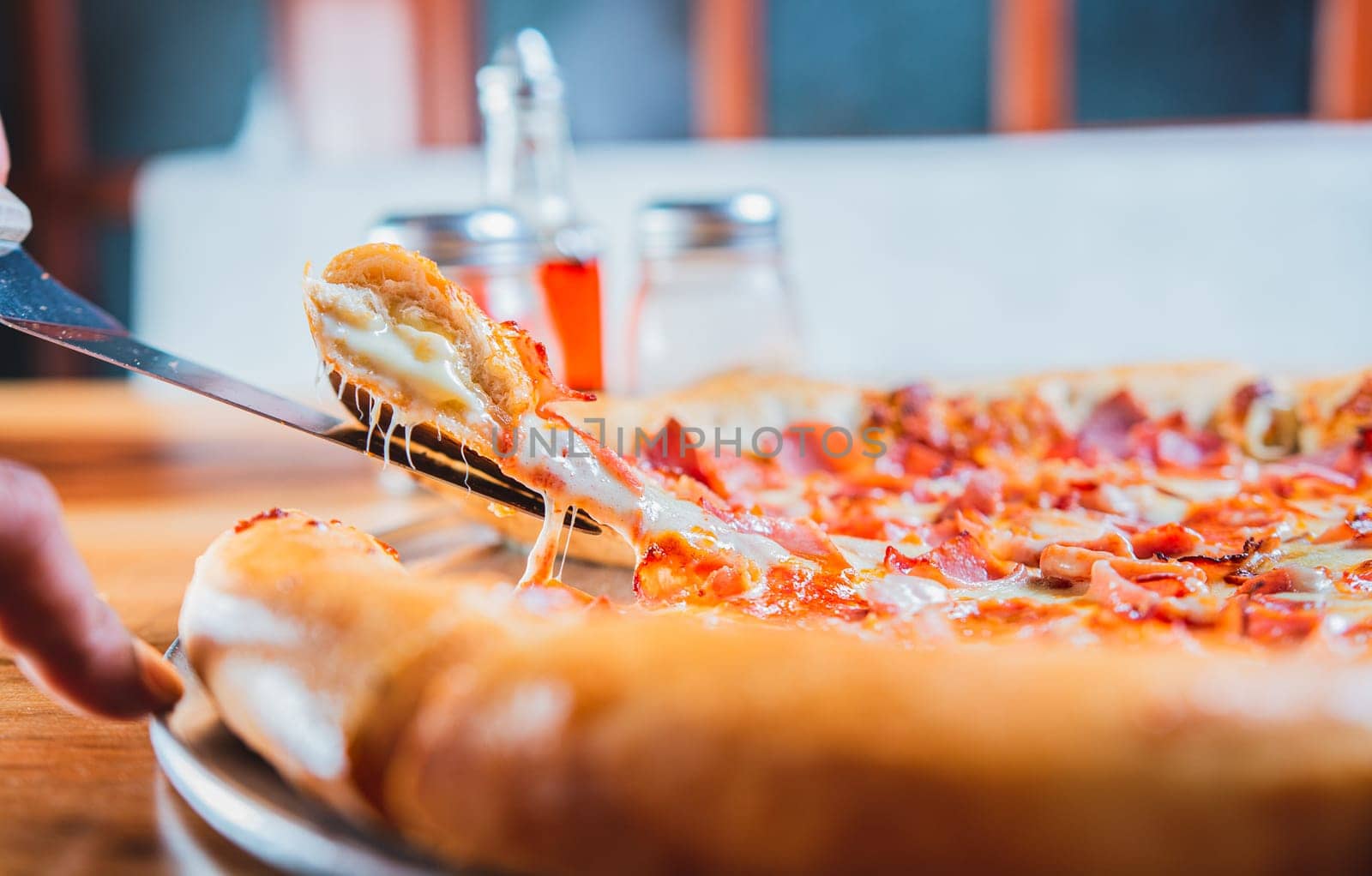 Homemade ham and cheese pizza with spatula on table. Hand taking a slice of ham pizza with the spatula by isaiphoto