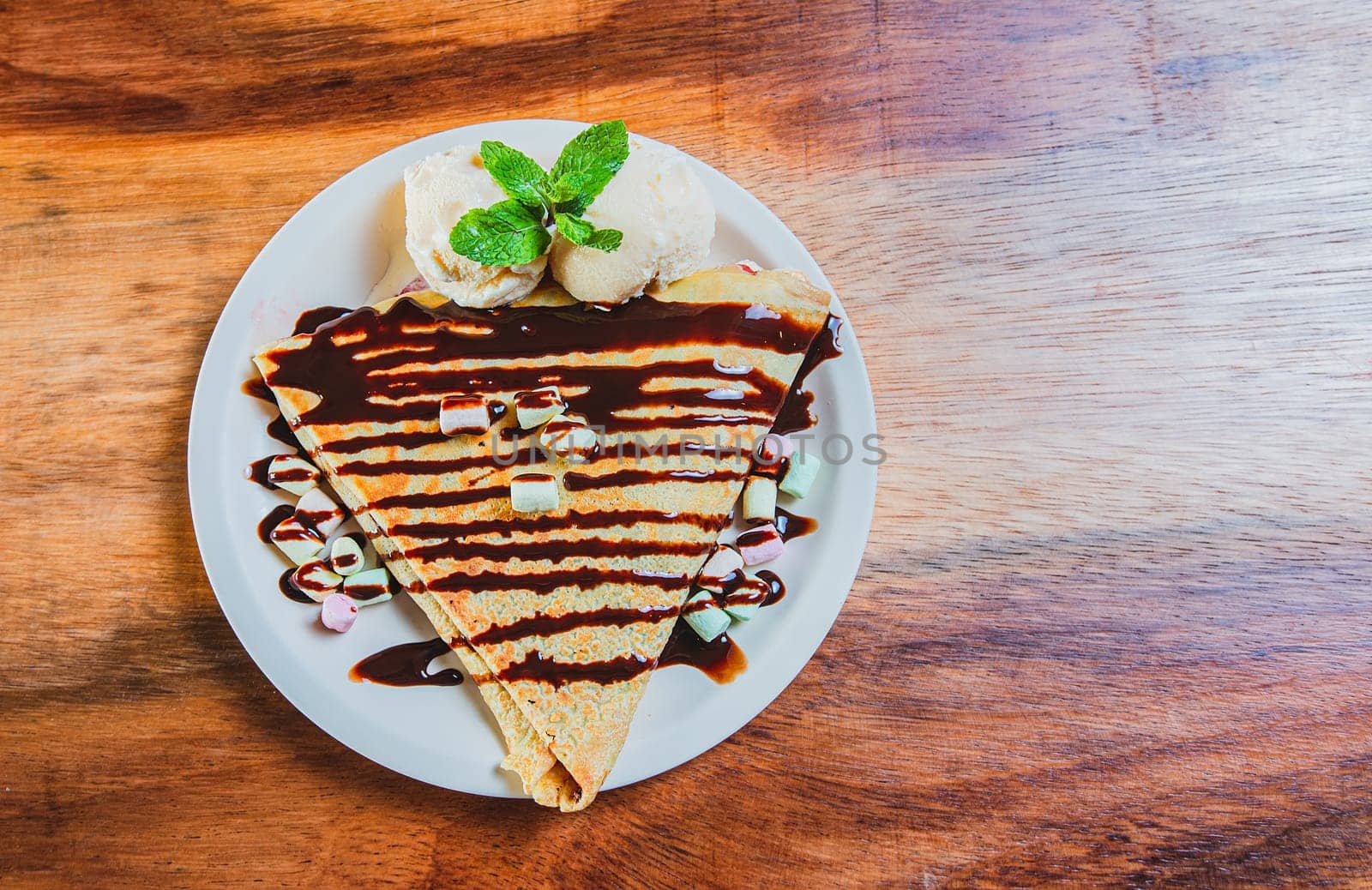 Top view of chocolate crepe with ice cream on wooden table. High angle view of chocolate crepe with ice cream on wooden background