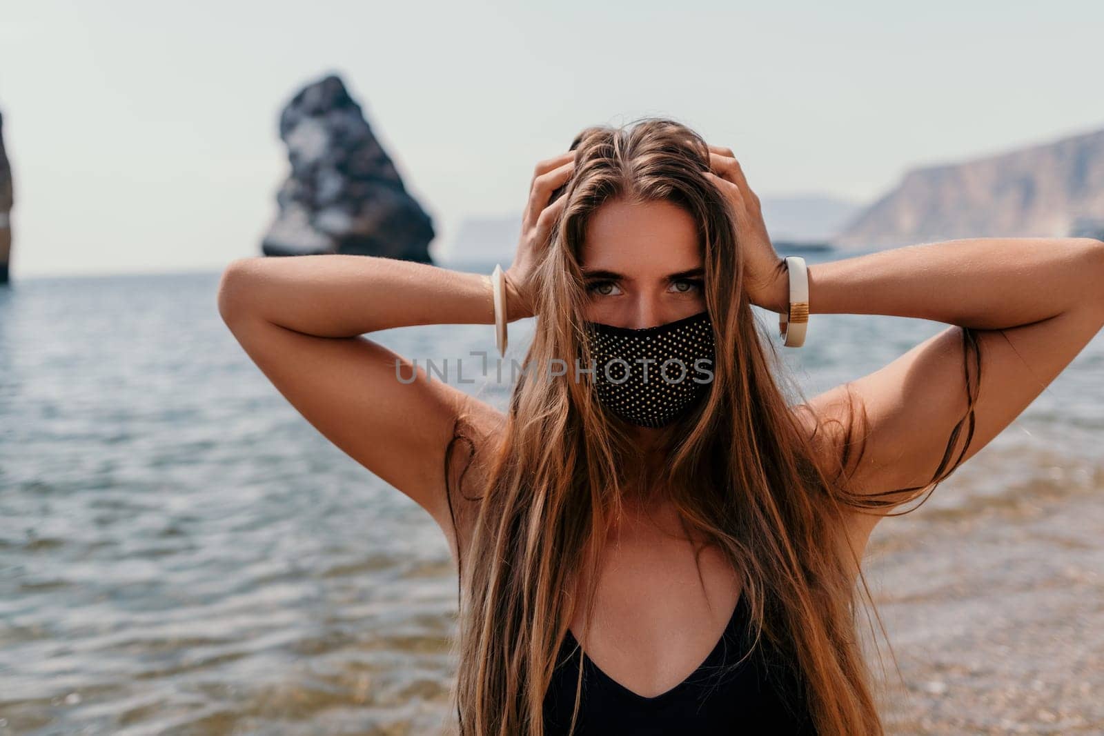 Woman summer travel sea. Happy tourist in black mask enjoy taking picture outdoors for memories. Woman traveler posing on the beach at sea surrounded by volcanic mountains, sharing travel adventure by panophotograph