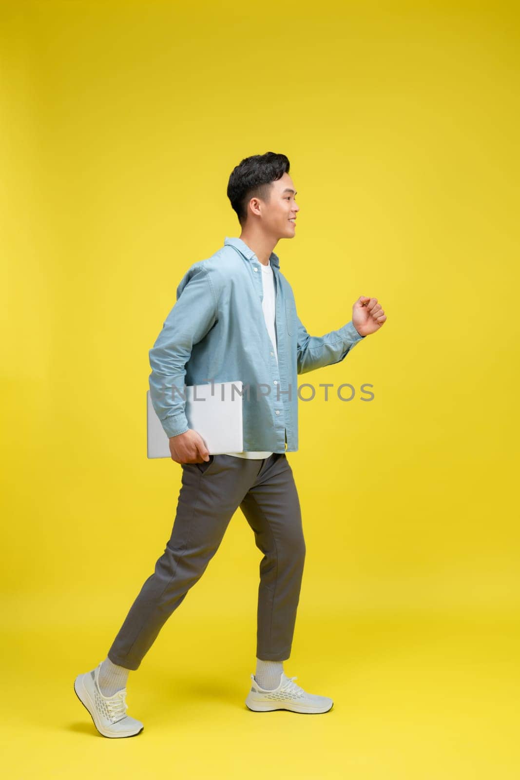 Smiling young Asian businessman shows laptop on isolated yellow background