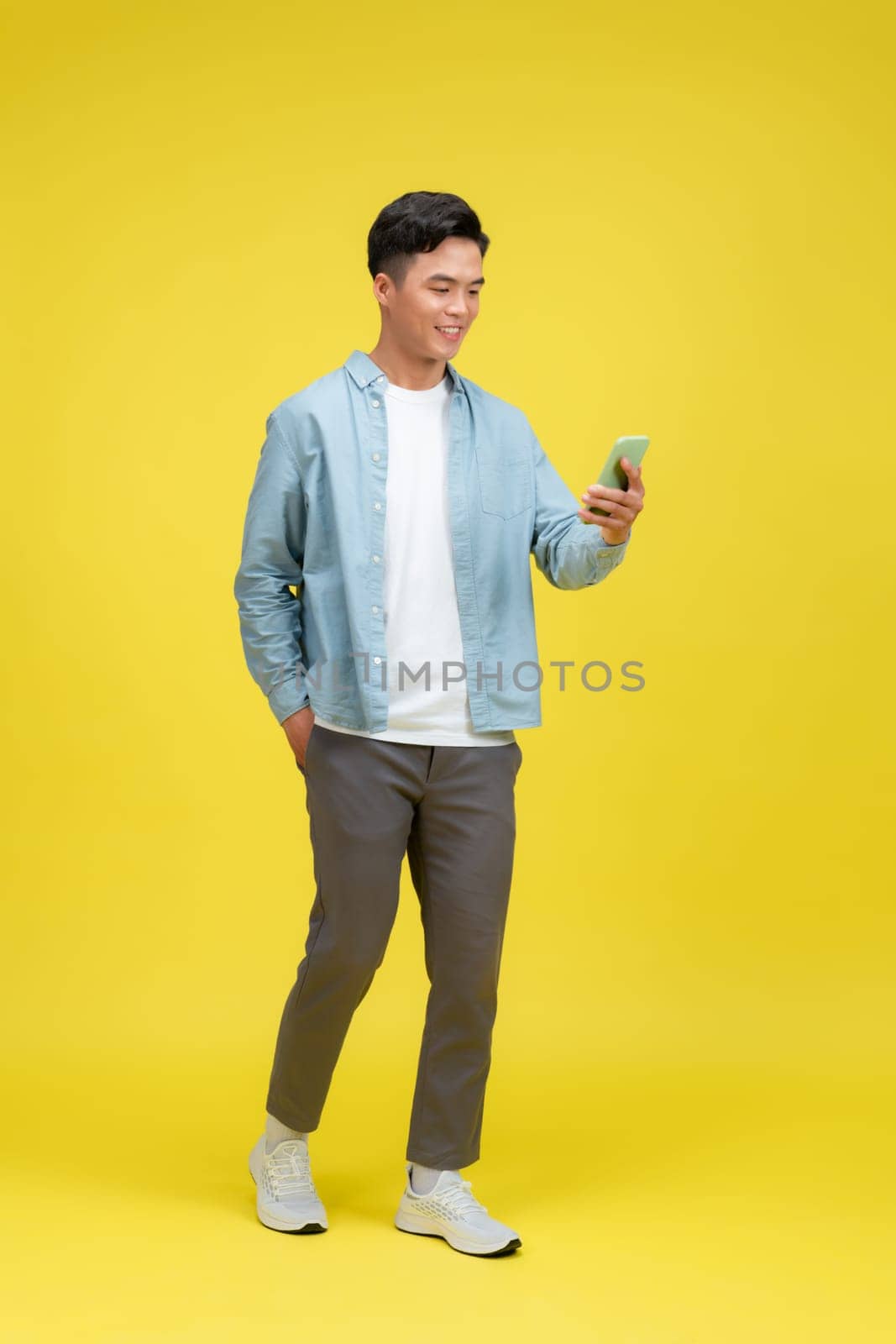 Adult Asian man walking relax while looking to the camera and holding mobile phone