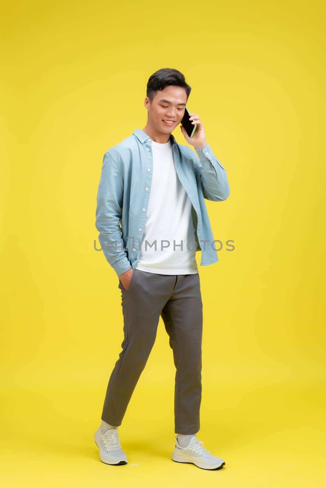 Happy smiling man in jeans and denim shirt talking on the phone looking at camera. 