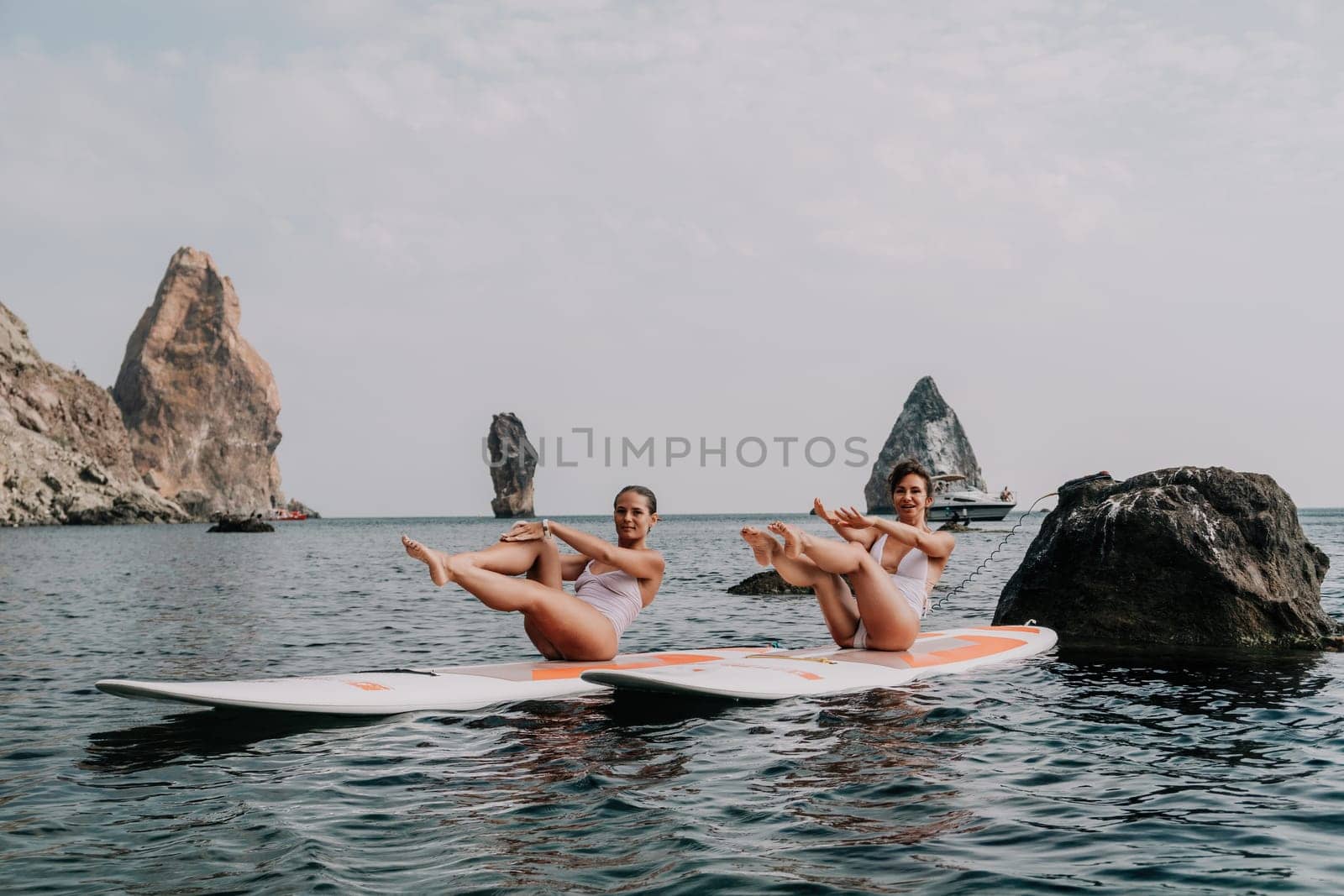 Woman sup yoga. Middle age sporty woman practising yoga pilates on paddle sup surfboard. Female stretching doing workout on sea water. Modern individual hipster outdoor summer sport activity