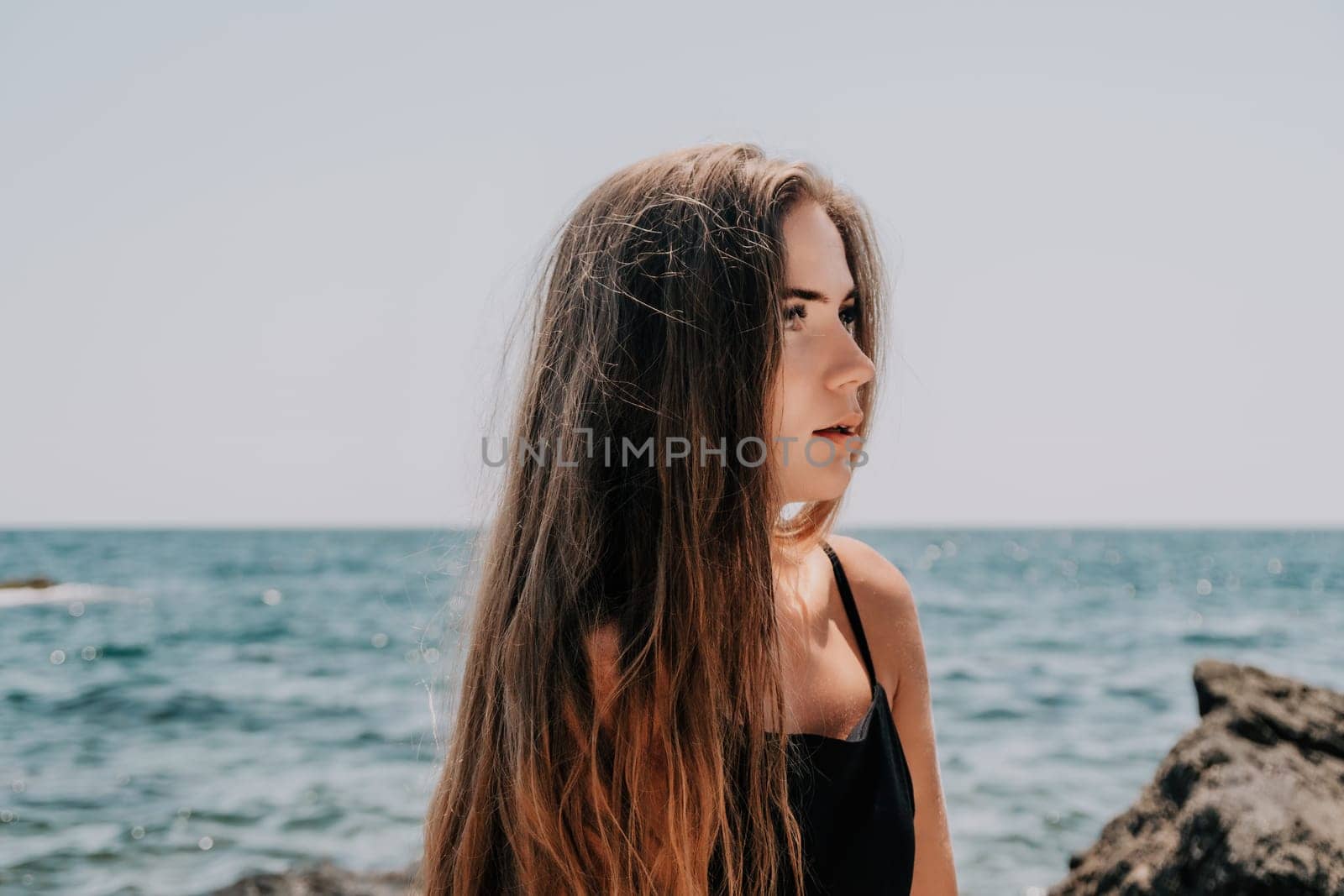 Woman travel sea. Young Happy woman in a long red dress posing on a beach near the sea on background of volcanic rocks, like in Iceland, sharing travel adventure journey