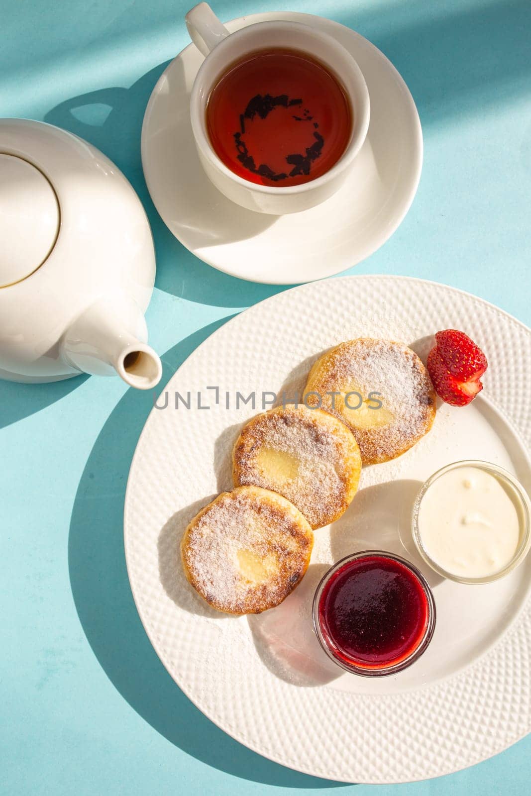 top view of a delicious morning breakfast on a blue background, cheesecakes and tea in the sun.