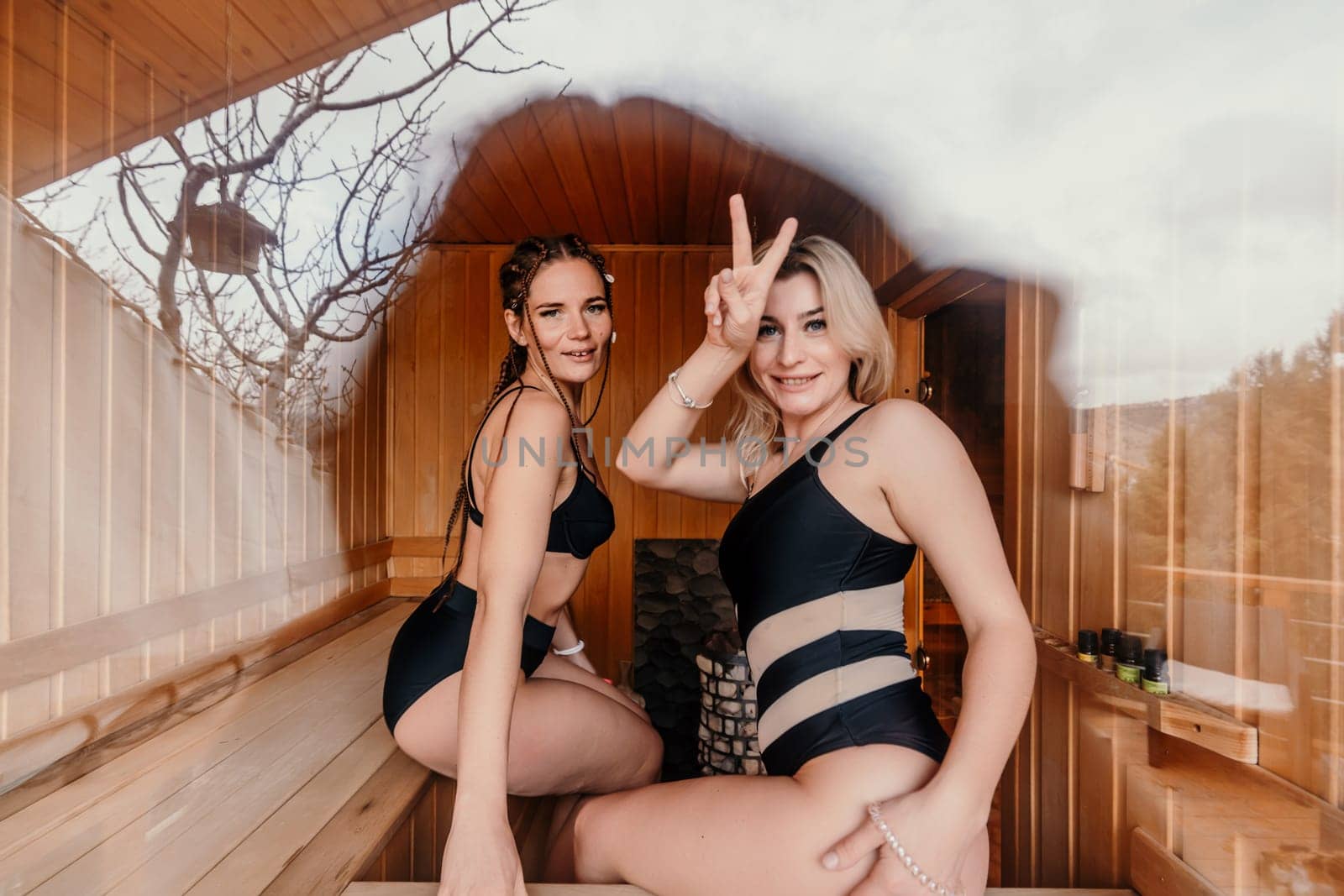 Sauna friend. Two women are sitting in a sauna in black bathing suits and talking to each other