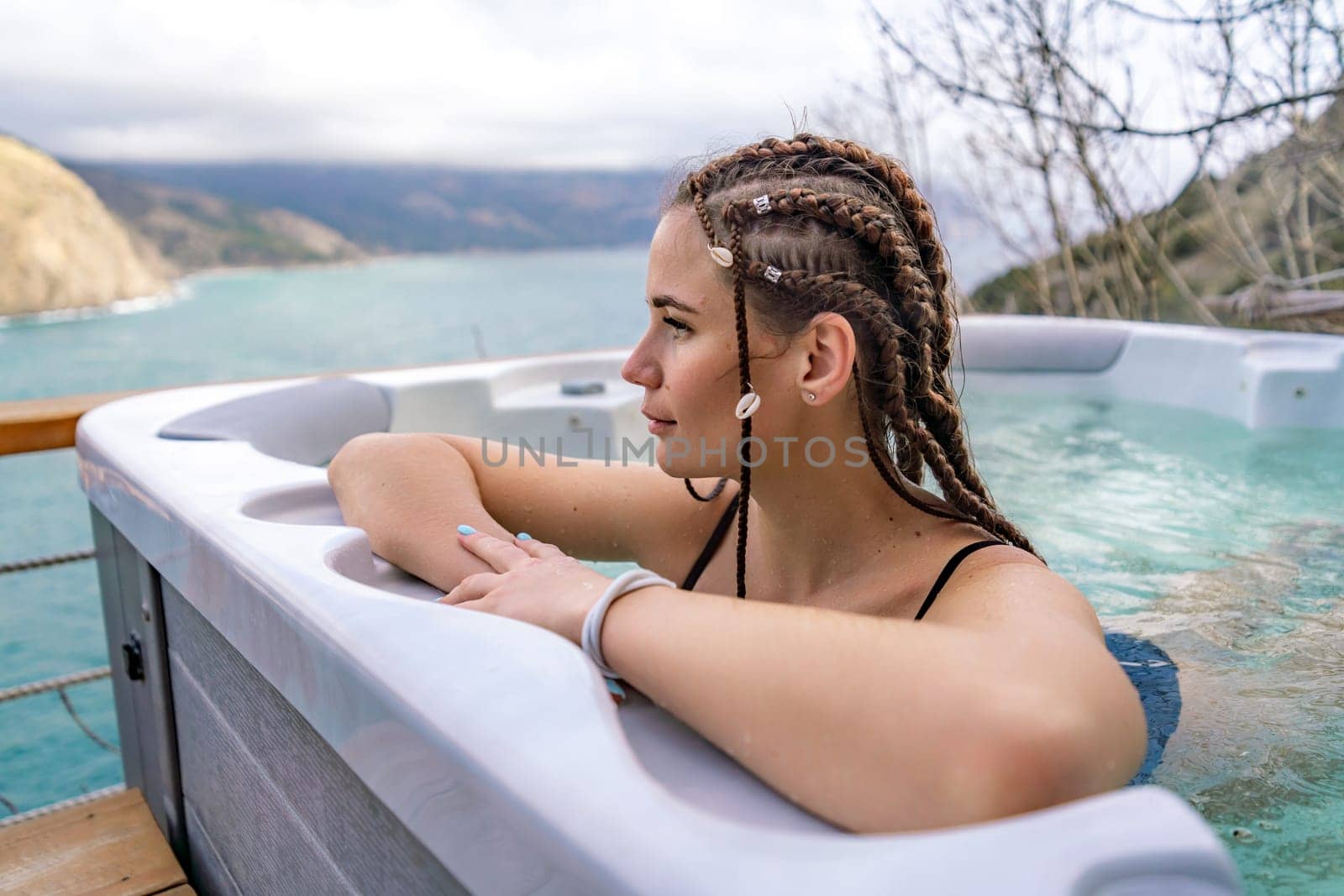 Take time for yourself. Outdoor swimsuit with mountain and sea views. A woman in a black swimsuit is relaxing in the hotel pool, admiring the view.