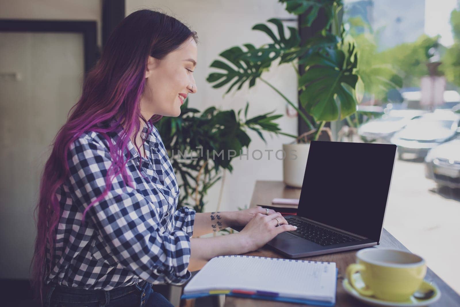 Rear shot of female student learning online via laptop before her lectures. Woman typing on notebook with blank screen with copy space for your text or advertising content, sitting at wooden table