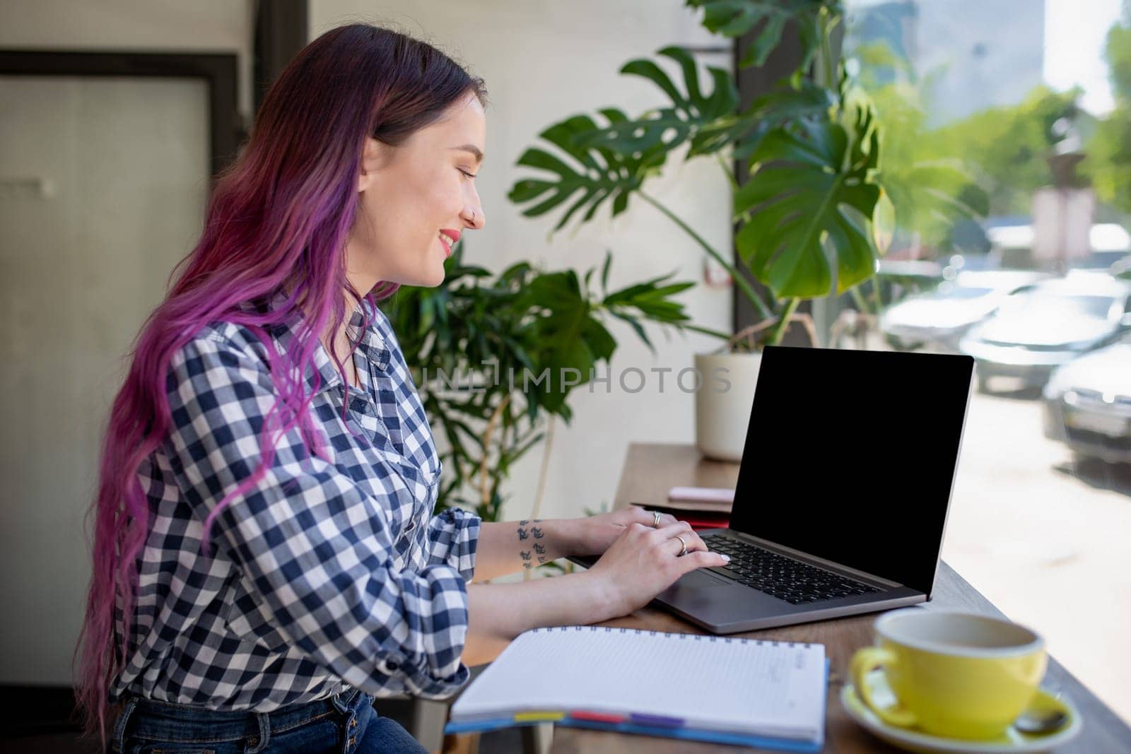 Rear shot of female student learning online via laptop before her lectures. Woman typing on notebook with blank screen with copy space for your text or advertising content, sitting at wooden table