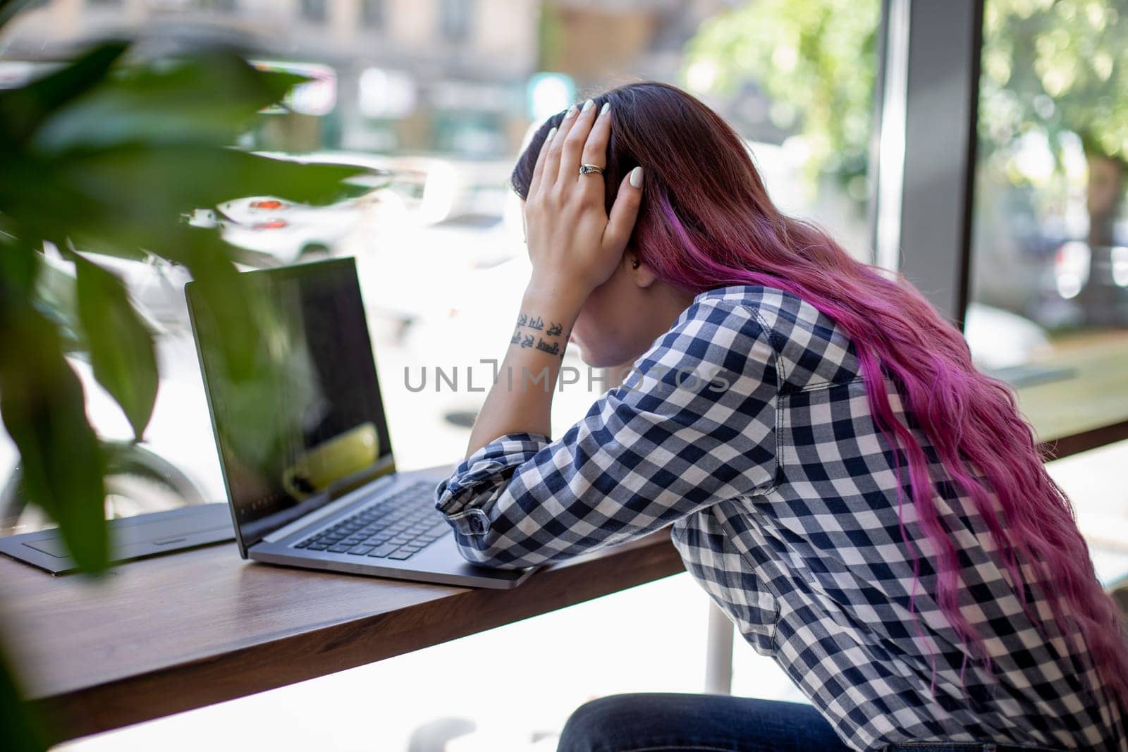 Rear shot of female student learning online via laptop before her lectures. Woman typing on notebook with blank screen, sitting at wooden table