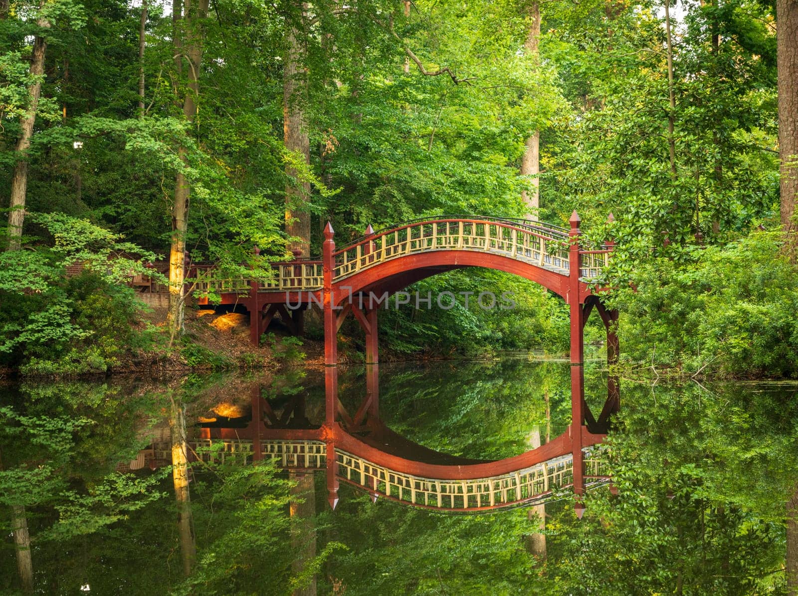 Ornate wooden bridge over very calm Crim Dell pond on campus of William and Mary college in Williamsburg Virginia