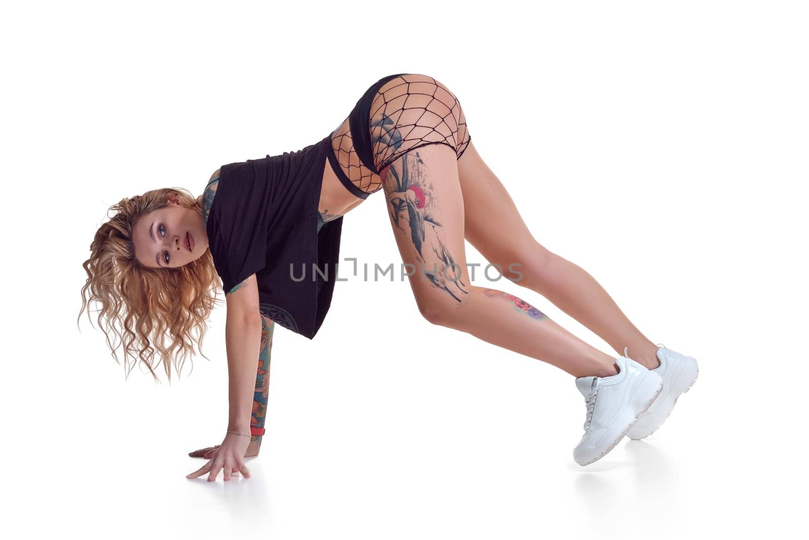 Young beautiful caucasian blonde girl with tattoo on her legs, wearing black booty shorts and fishnet dancing twerk isolated on white background