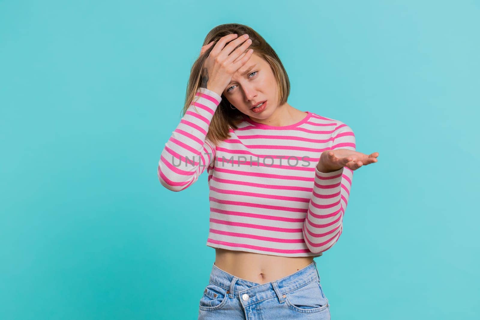 Face palm. Shame on you. Upset Caucasian young woman making face palm gesture, feeling bored, disappointed in result, bad news, sorrowful. Unhappy girl isolated on blue studio background indoors