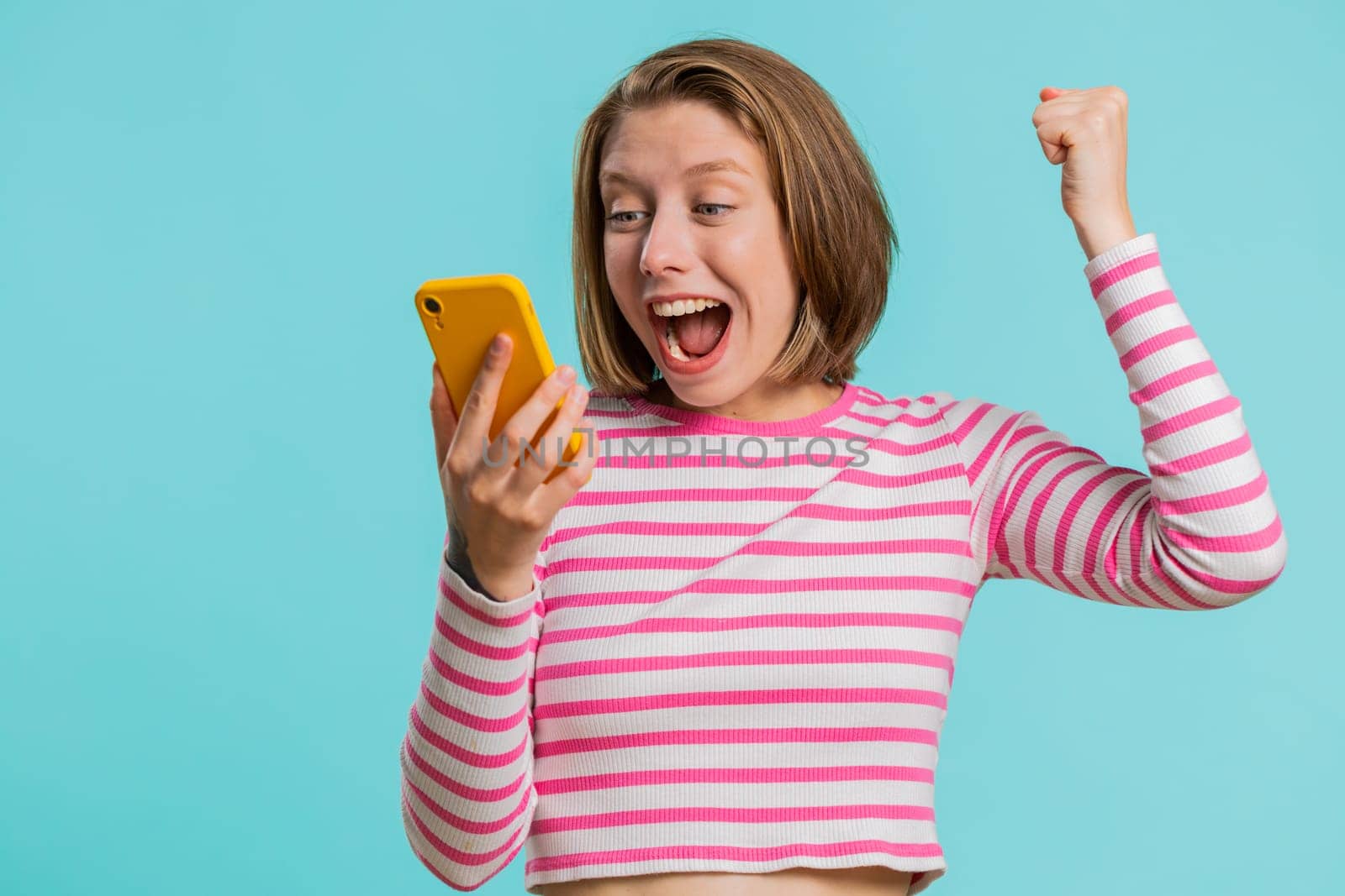Happy excited joyful woman girl use smartphone typing browsing shouting say wow yes found out great big win, good news, lottery goal achievemen, celebrating success, winning game on blue background