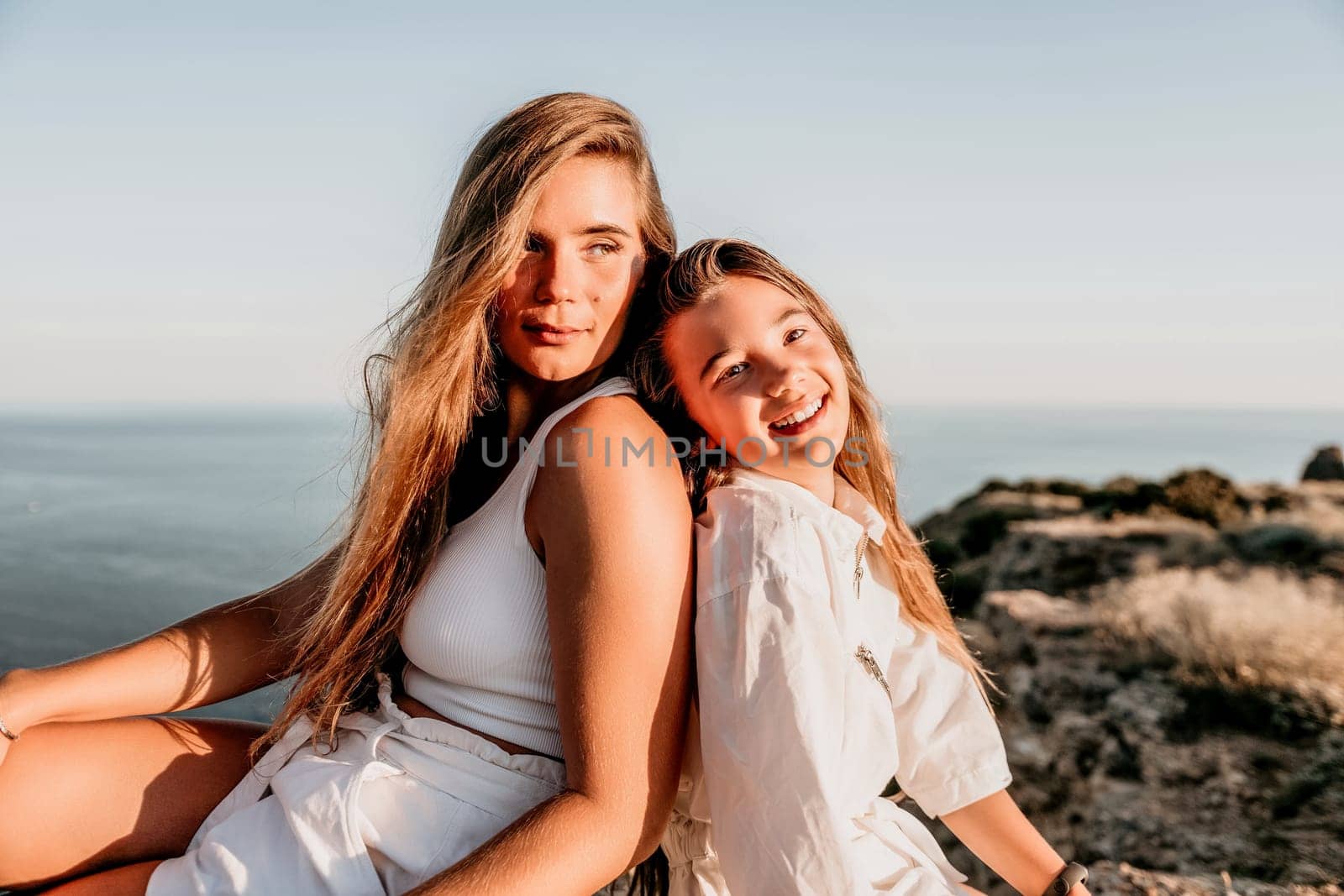 Sea family vacation together, happy mom and teenage daughter hugging and smiling together over sunset sea view. Beautiful woman with long hair relaxing with her child. Concept of happy friendly family. by panophotograph