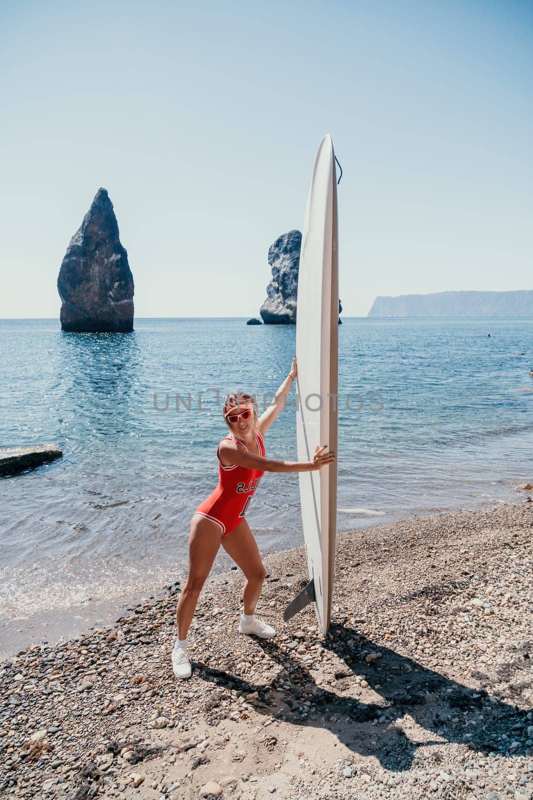 Woman sea sup. Close up portrait of happy young caucasian woman with blond hair looking at camera and smiling. Cute woman portrait in red bikini posing on sup board in the sea by panophotograph