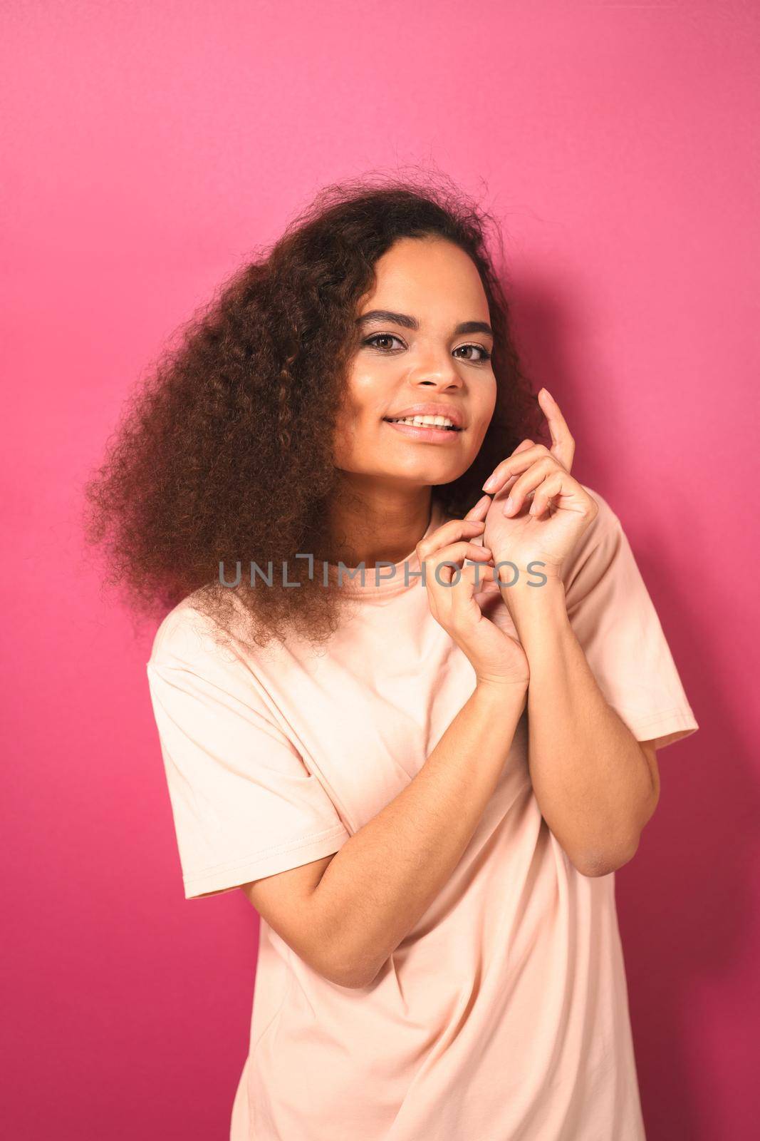 Beautiful dark skinned African American young girl looking gently at camera wearing peachy t-shirt isolated on pink background. Beauty concept. Facial expressions, emotions, feelings.