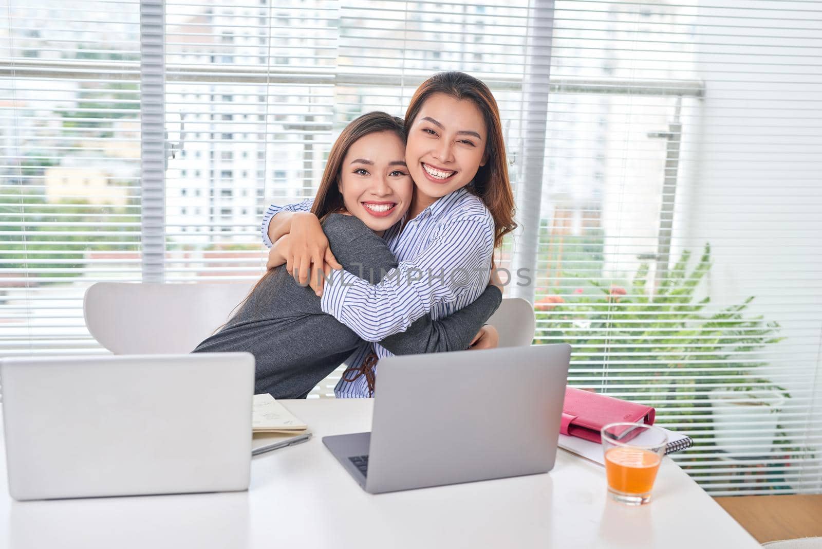 Indoor portrait of smiling girls working together in office. Pretty woman spending time with friend during break and posing for photo in library.