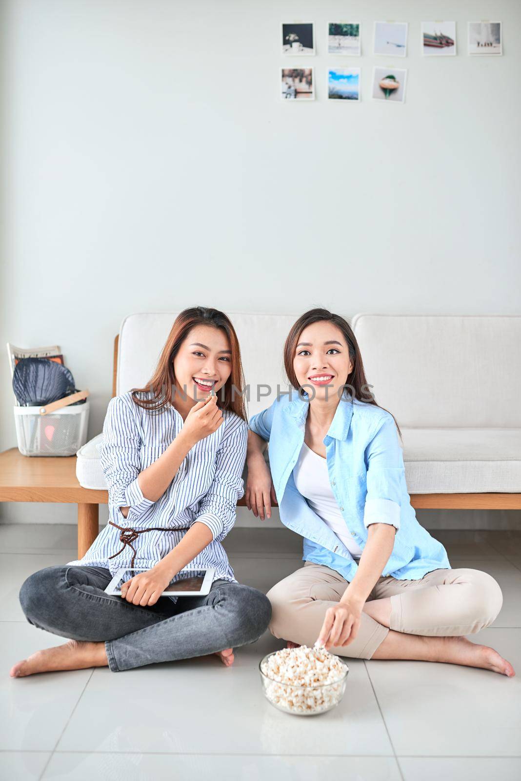 Wondered amazed impressed girl gesturing forefinger eating popcorn watching funny comic program with her friend sitting in living room indoor enjoying interesting film by makidotvn