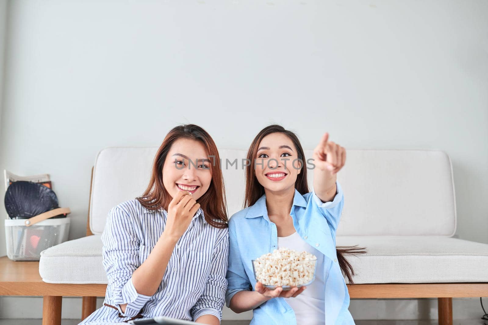 Wondered amazed impressed girl gesturing forefinger eating popcorn watching funny comic program with her friend sitting in living room indoor enjoying interesting film by makidotvn