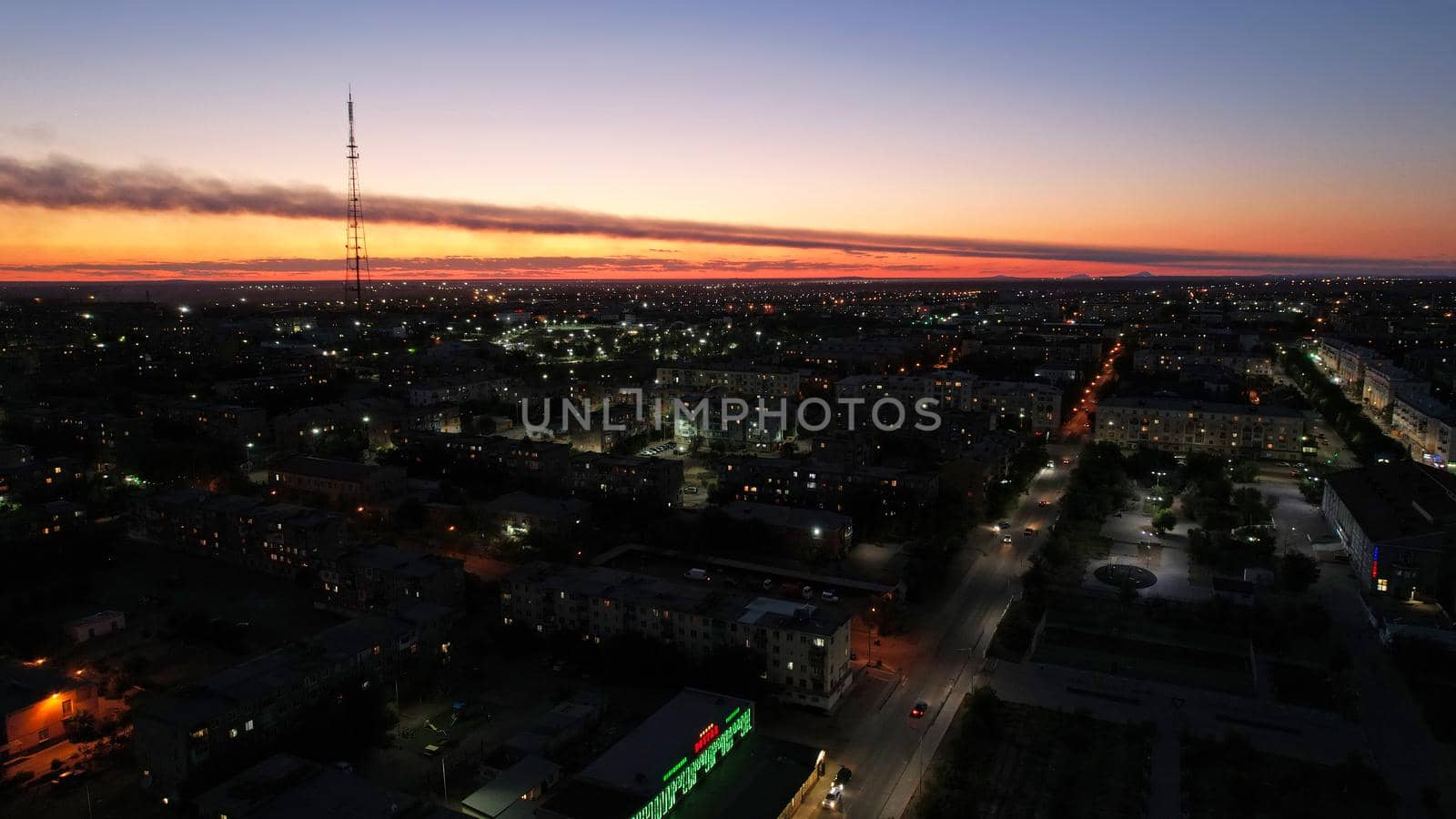 The outskirts of the city. There are old houses, garages and fences. In the distance, you can see the TV tower and the city. Swifts fly. The sky is shimmering purple-blue. Shooting from a drone.