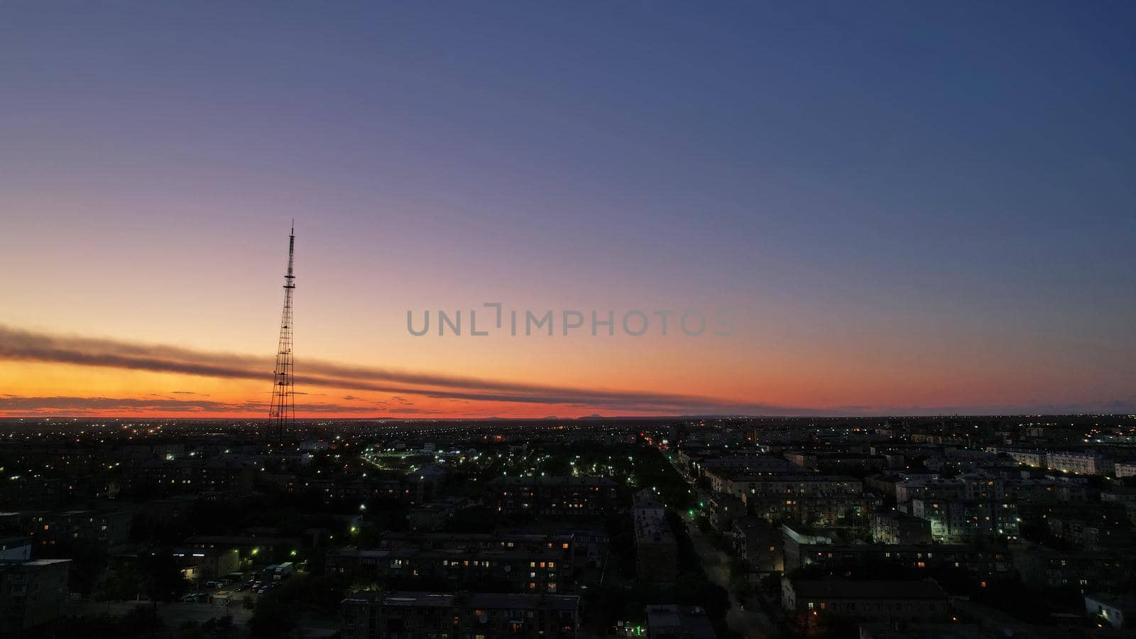 The outskirts of the city. There are old houses, garages and fences. In the distance, you can see the TV tower and the city. Swifts fly. The sky is shimmering purple-blue. Shooting from a drone.