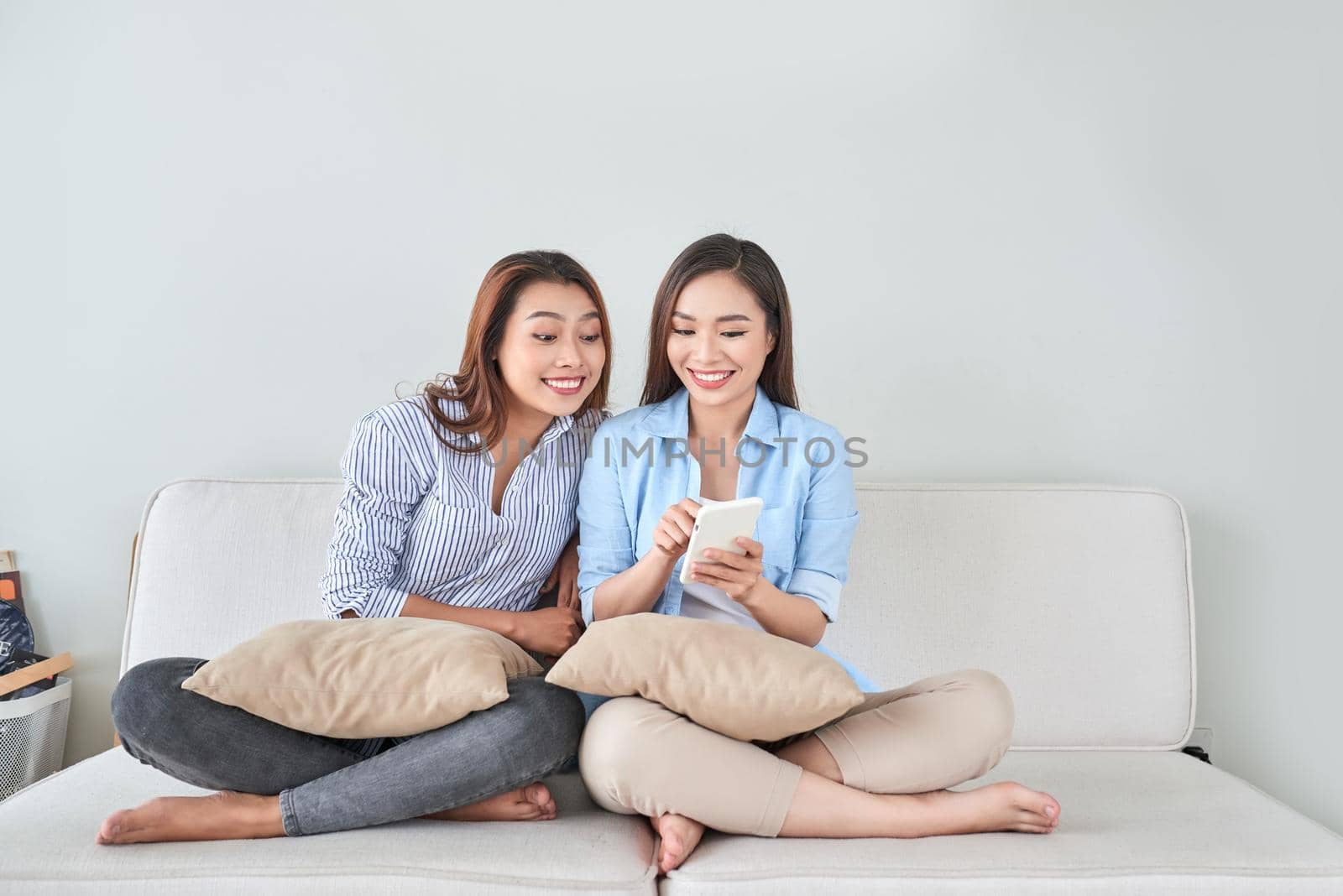 Close up portrait of two excited girlfriends with mobile phones, laughing. Happy joyful female friends resting at home, enjoying talks, having fun. by makidotvn