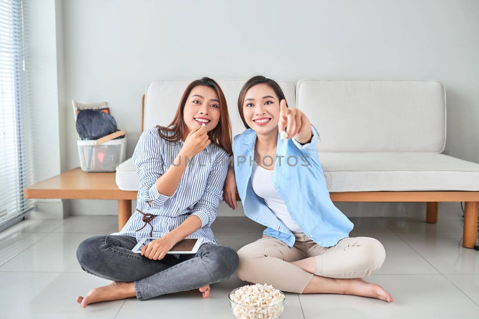 Wondered amazed impressed girl gesturing forefinger eating popcorn watching funny comic program with her friend sitting in living room indoor enjoying interesting film by makidotvn