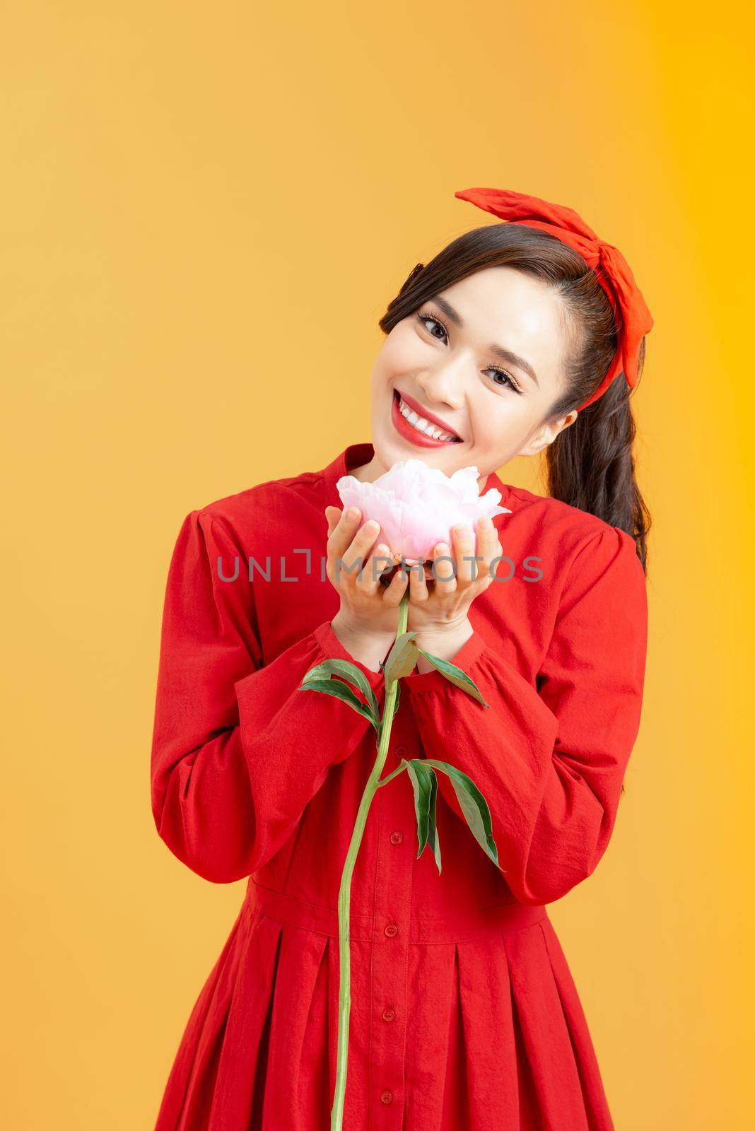 Portrait of an attractive young Asian woman in red dress holding peony flower isolated over orange background