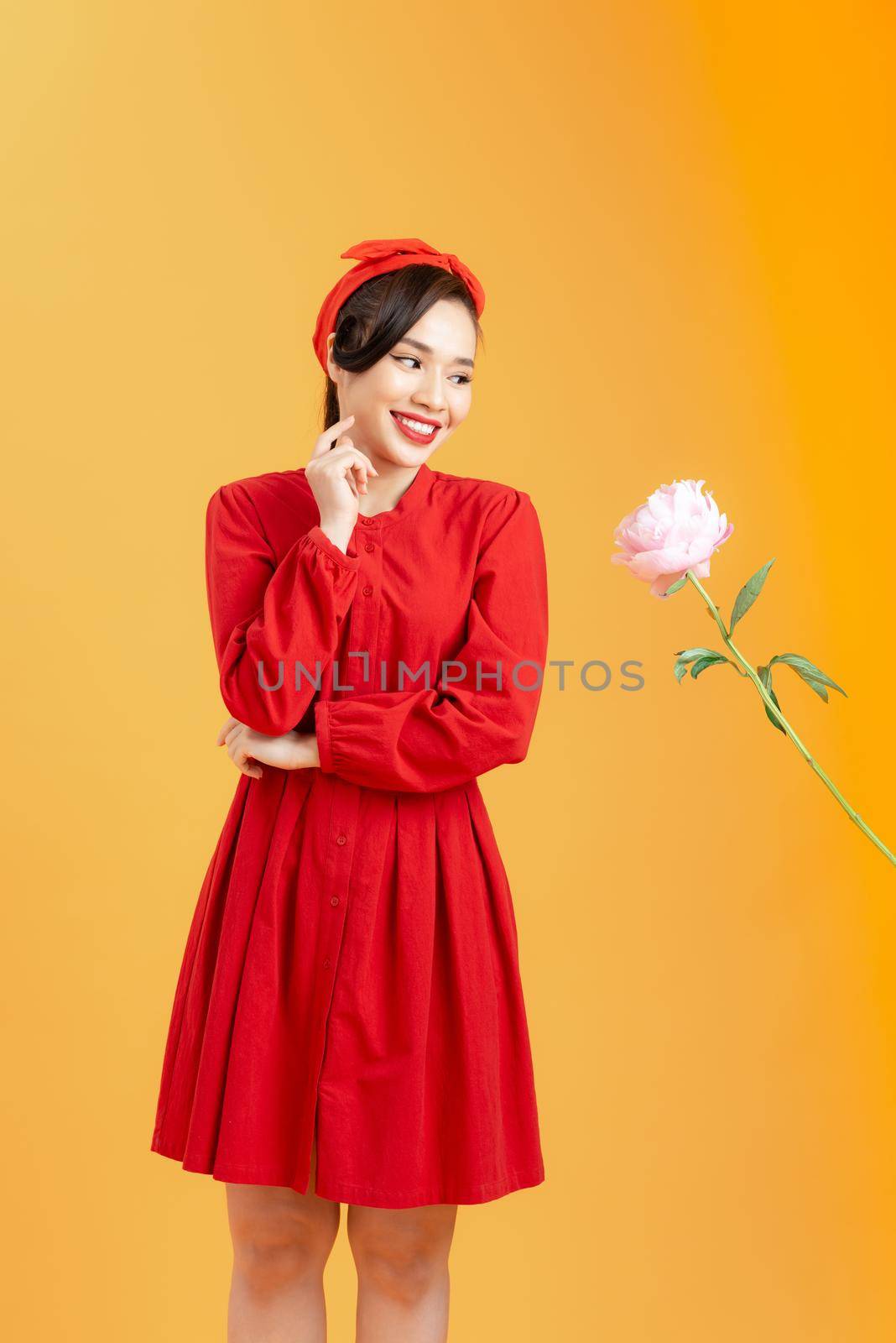 Young Asian woman happy to receive peony rose when standing isolated on orange background. by makidotvn