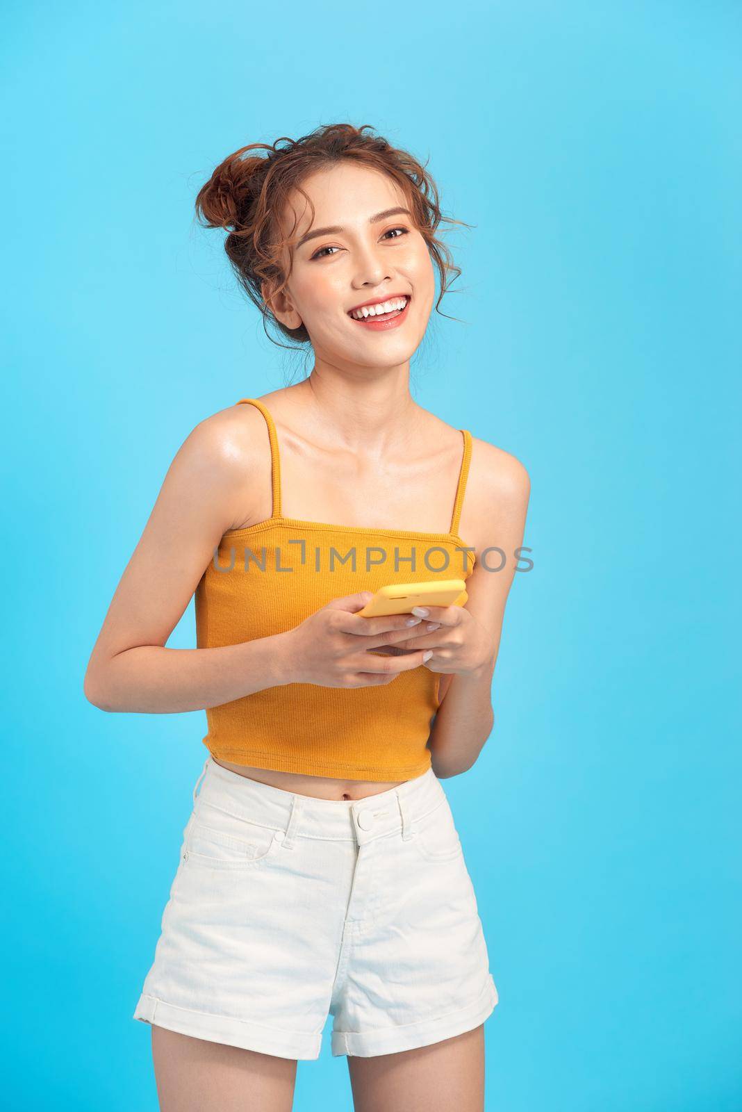 pretty smiling girl in summer clothes using mobile phone while standing 